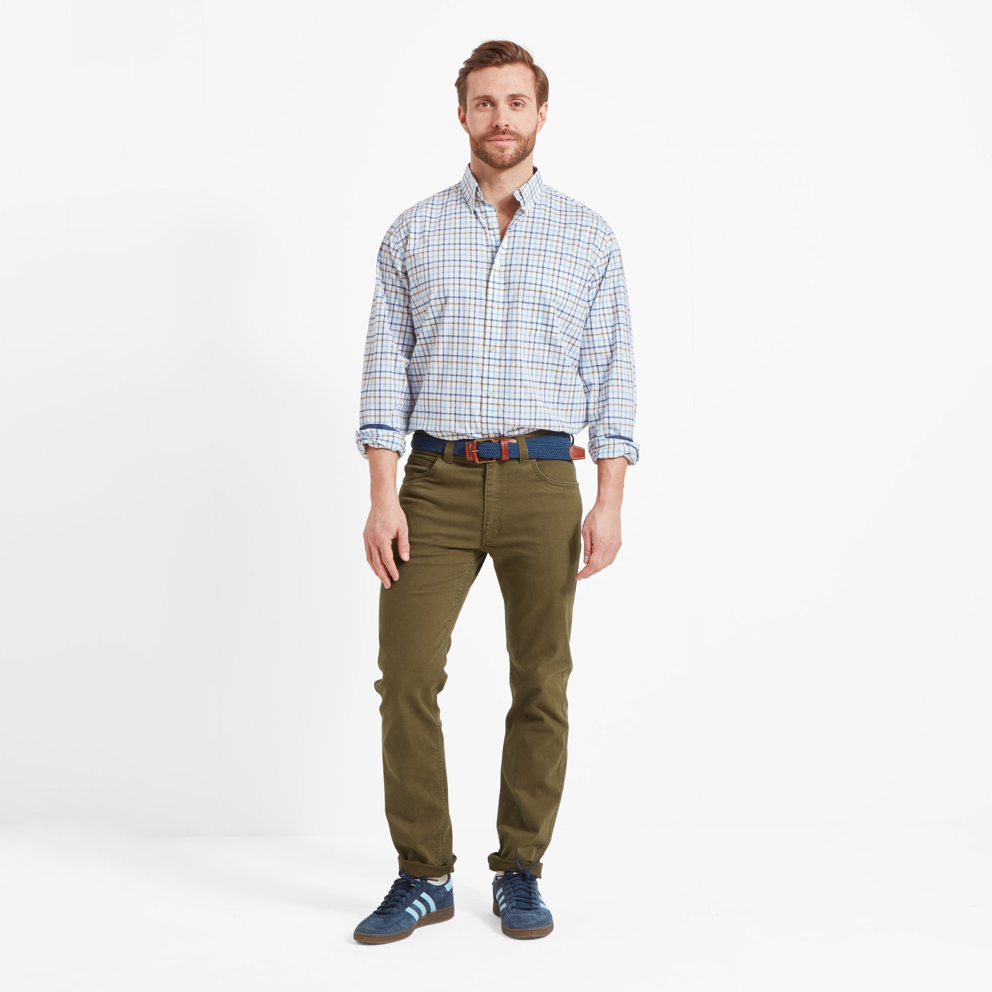 Man wearing a checked shirt, green jeans, and blue shoes against a white background
