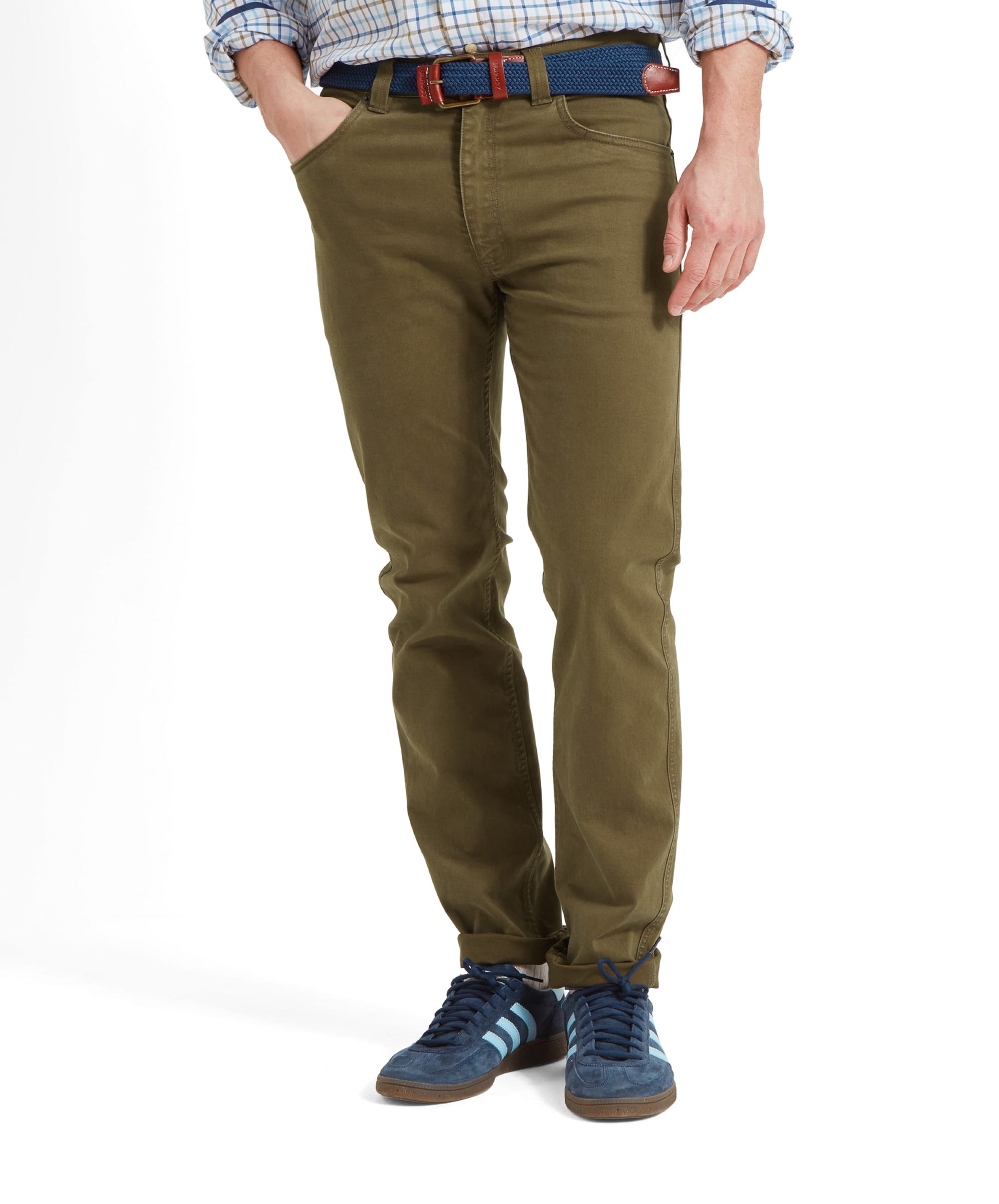 Person with their hand in their pocket wearing olive green jeans with a blue belt and shoes against a white background