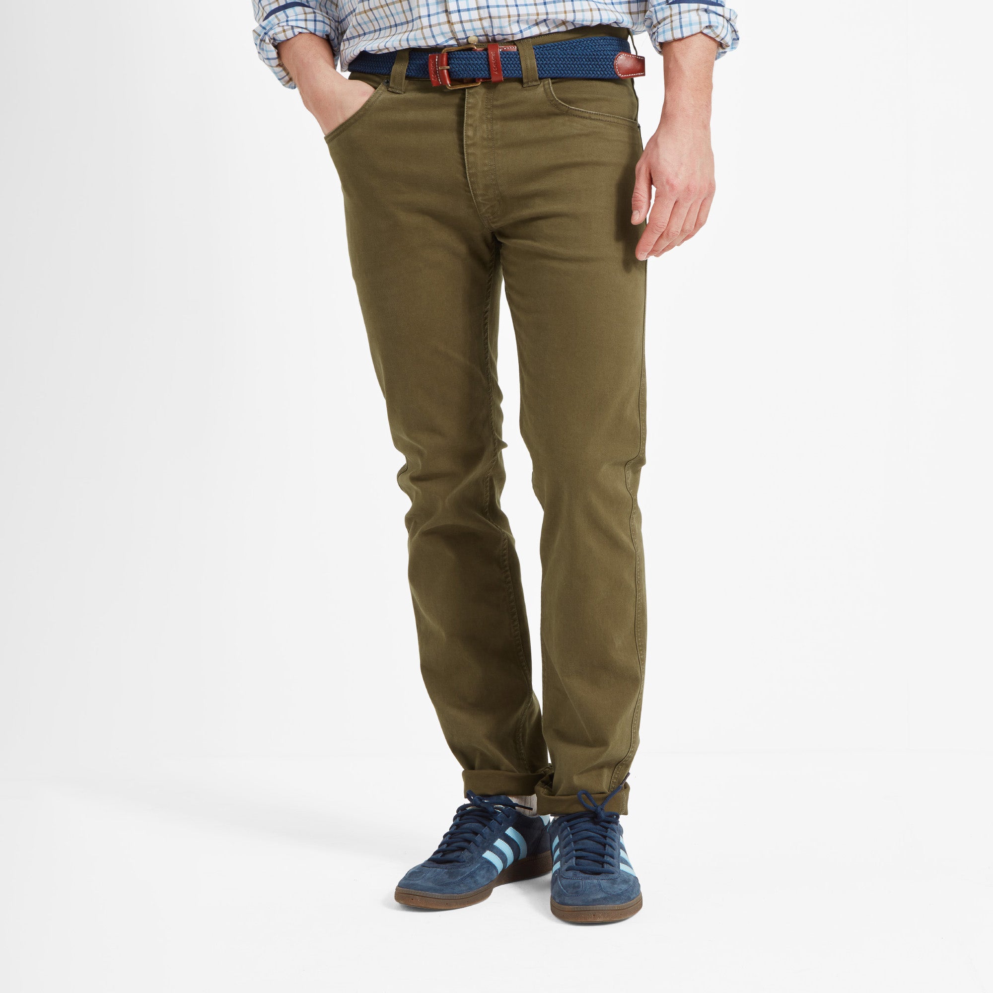 Person wearing olive green jeans with a blue belt and shoes against a white background
