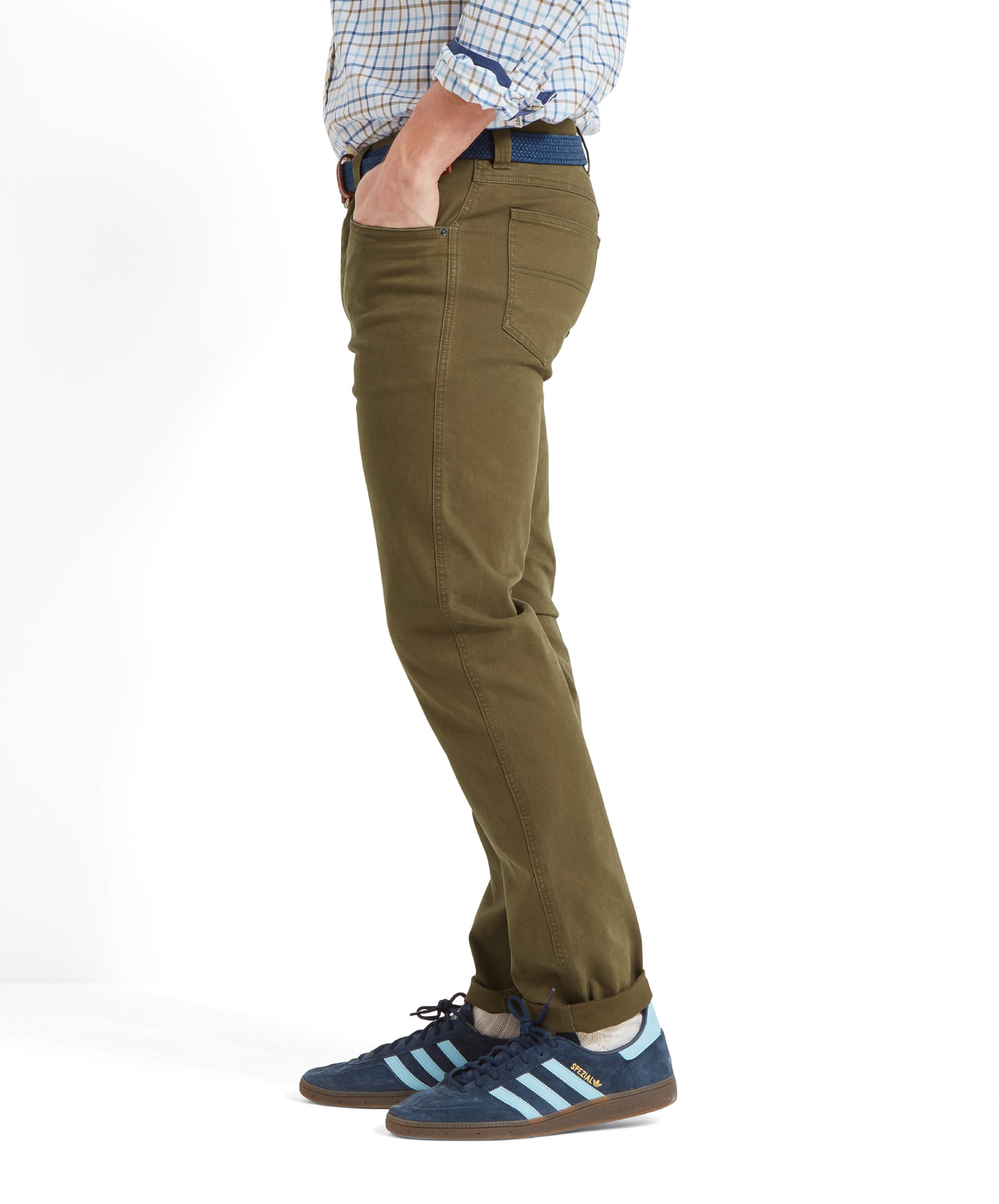 Person standing sideways wearing green jeans and blue trainers against a  white background