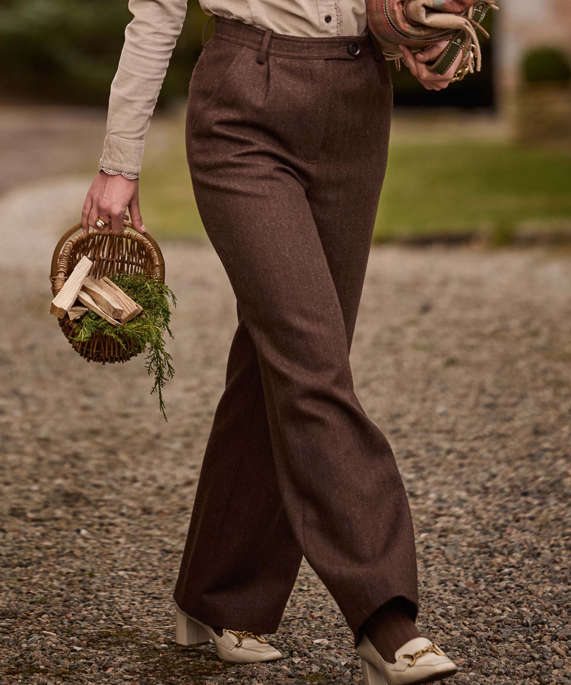 Woman walking in Schöffel Country's flared brown tweed trousers, carrying a wicker log basket