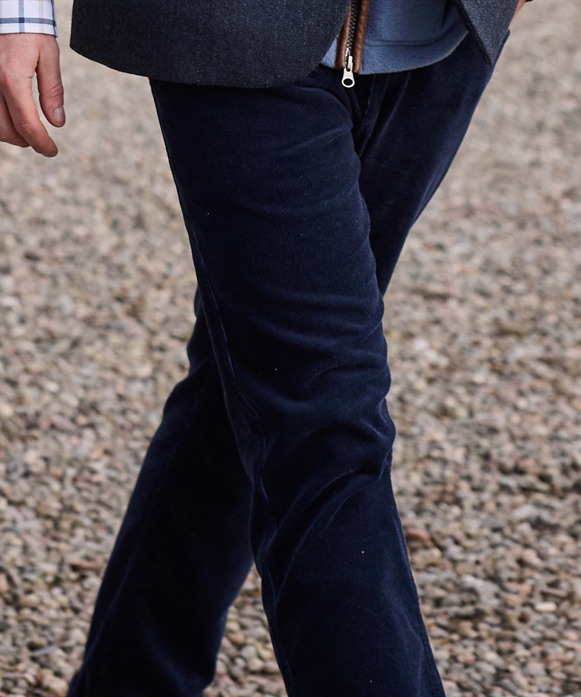 Close-up of Schöffel Country's navy corduroy flared trousers, worn with a grey tweed blazer, walking on gravel