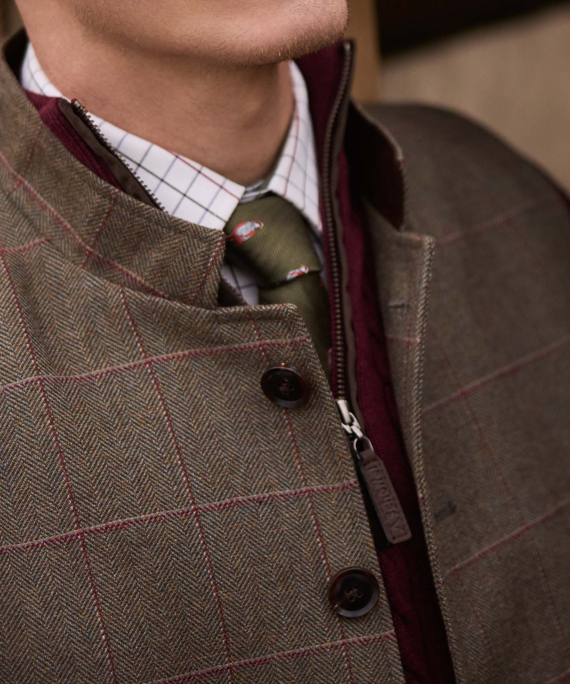 Close-up of the zip and button collar detail on Schöffel Country's tweed gilet, worn with an olive tie