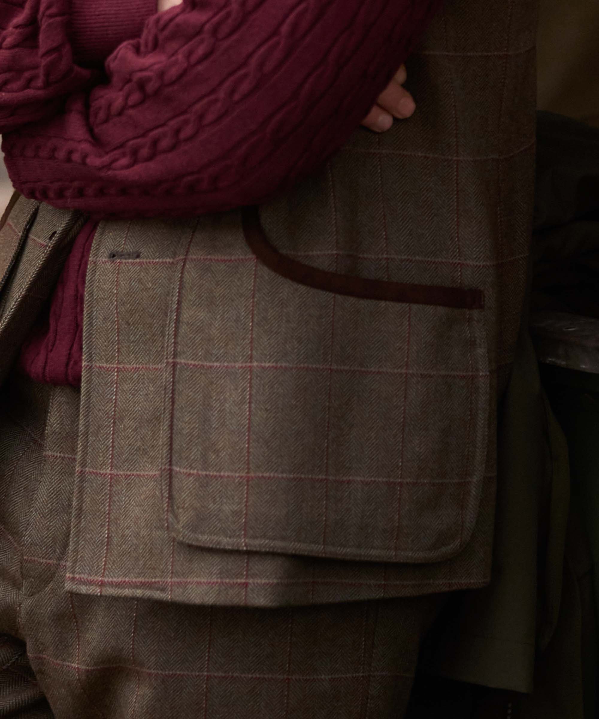 Close-up of the leather-trimmed pocket on Schöffel Country's tweed gilet, worn over a burgundy cable knit jumper