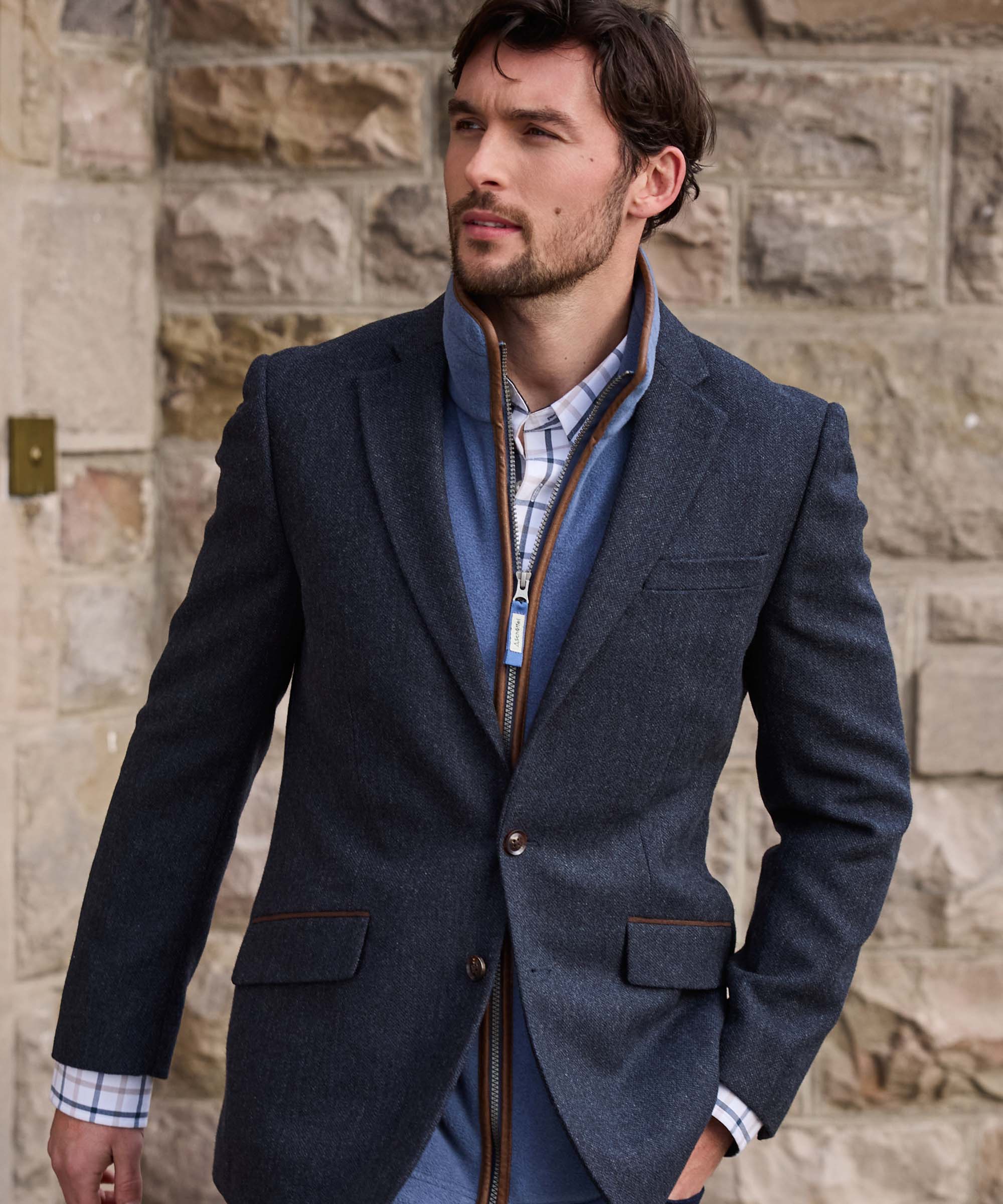 Man wearing Schöffel Country's navy herringbone tweed blazer with leather-trimmed zip gilet and check shirt