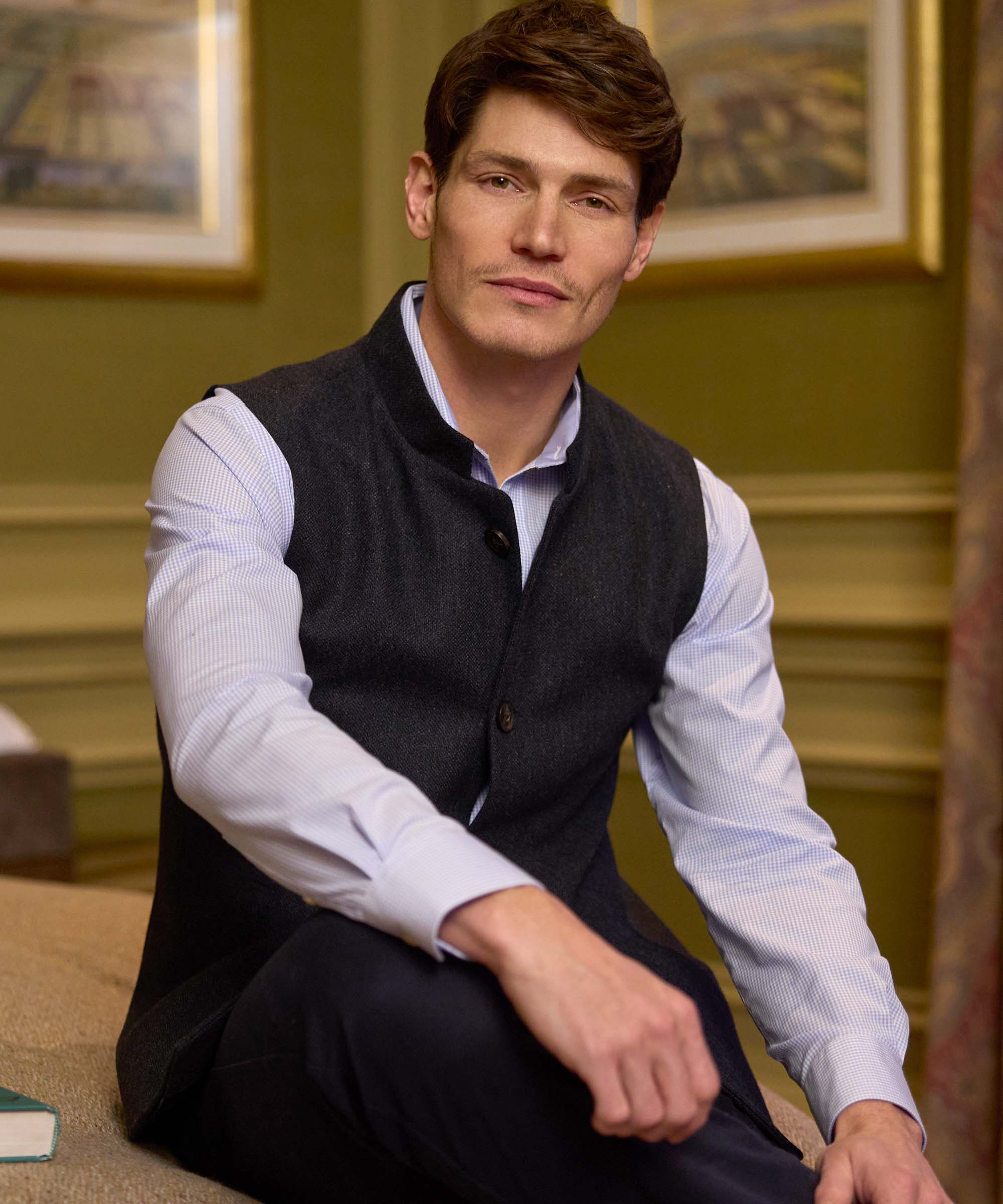 Man wearing Schöffel Country's charcoal wool gilet with stand collar, seated with a book