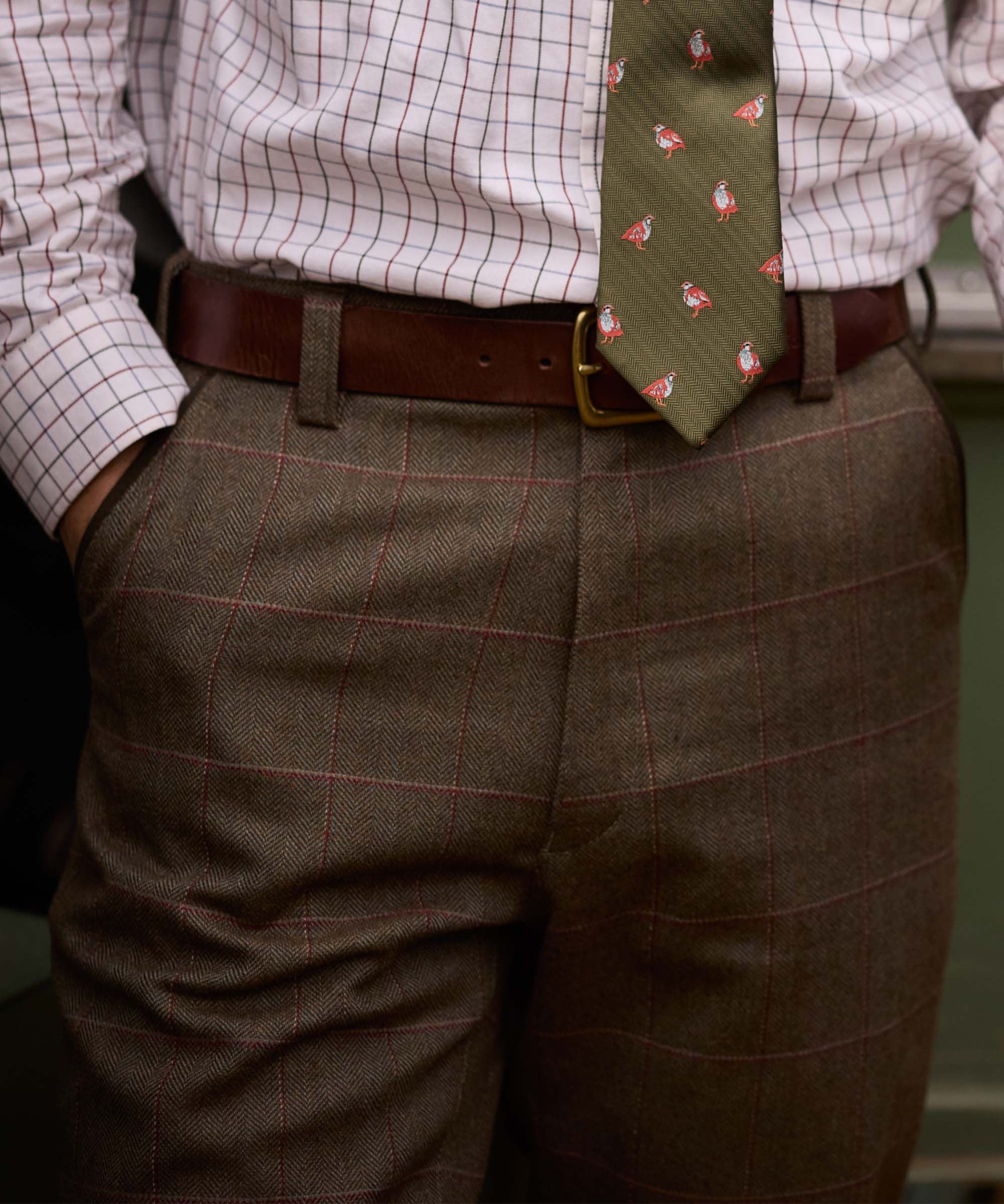 Close-up of Schöffel Country's herringbone tweed trousers, worn with a game bird print tie and leather belt
