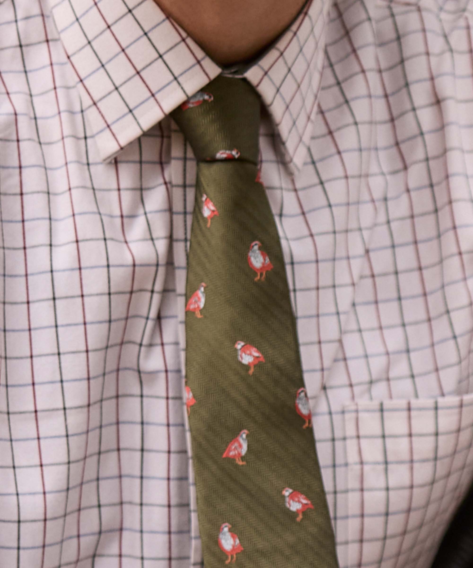 Close-up of Schöffel Country's olive game bird print silk tie, knotted with a check shirt