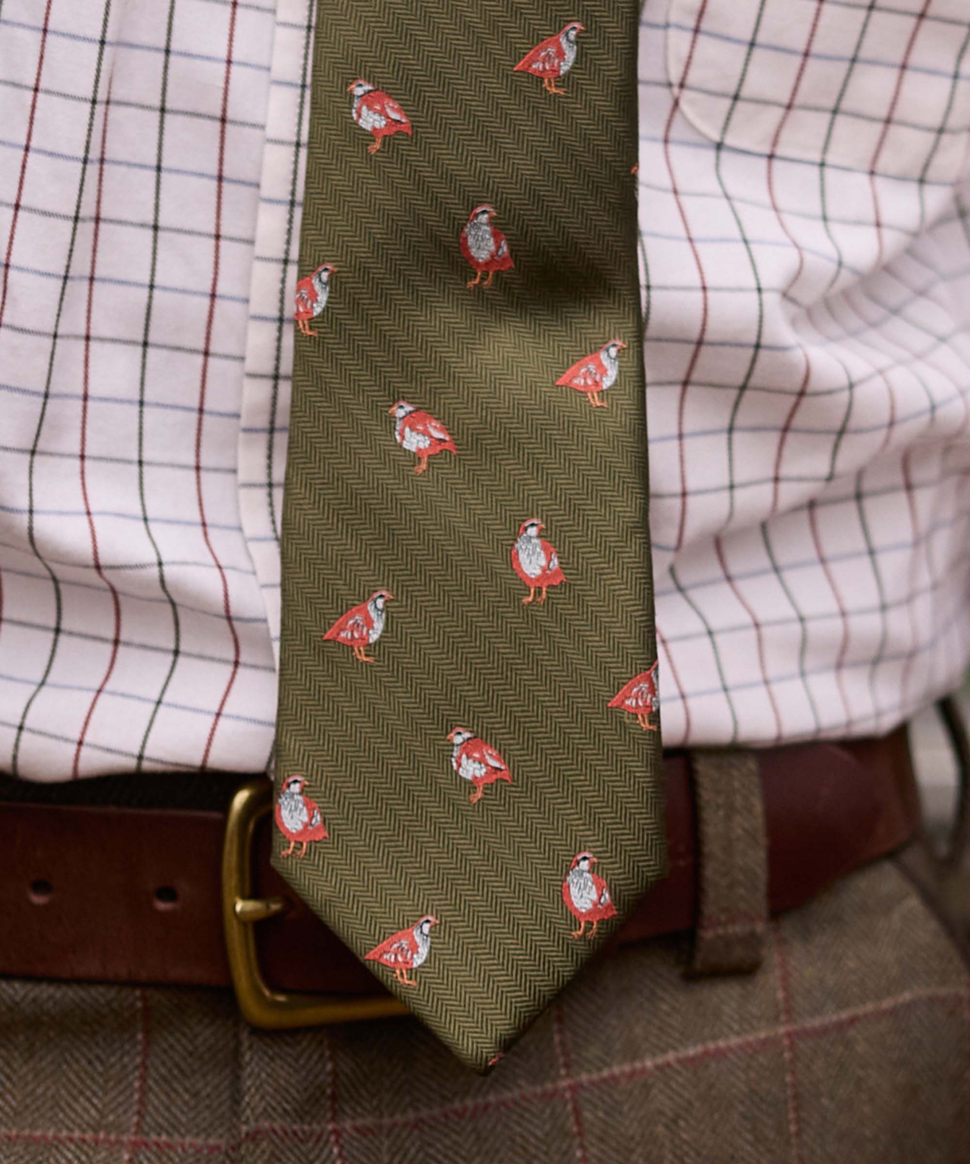 Close-up of Schöffel Country's olive game bird print silk tie, worn with a tweed belt and check shirt
