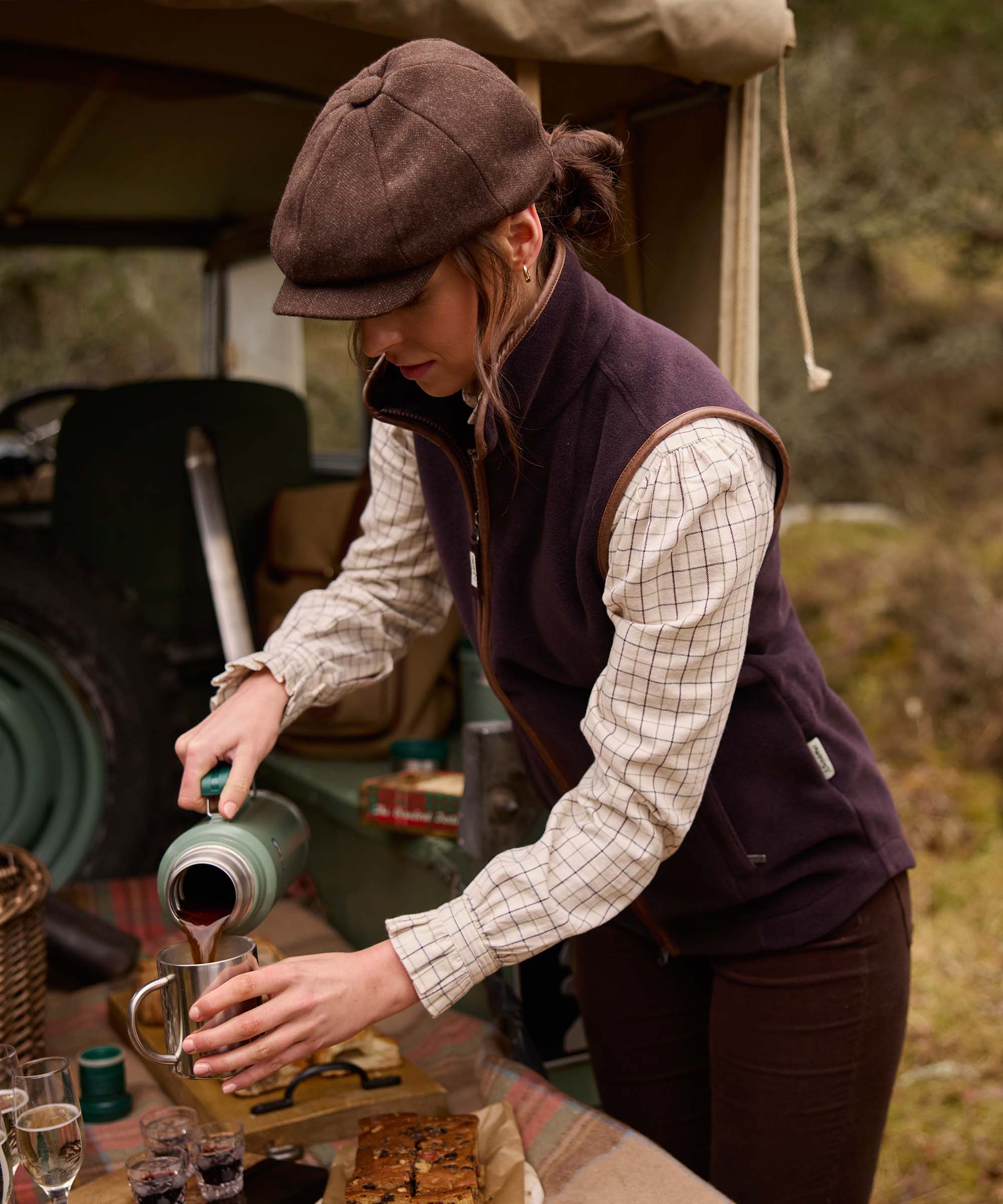 Woman wearing Schöffel Country's aubergine fleece gilet, pouring coffee from a flask outdoors