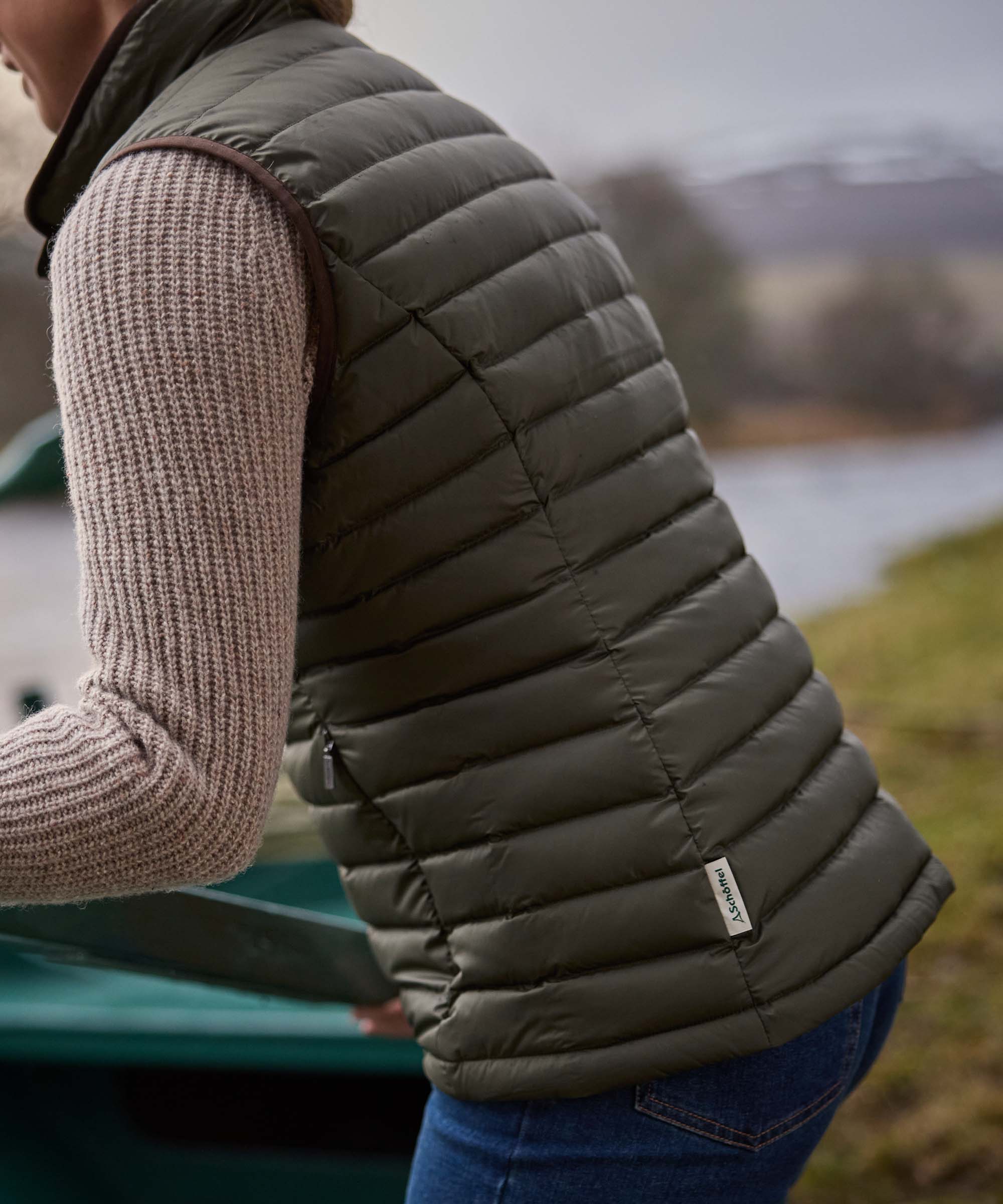Close-up of an olive green Schöffel quilted gilet shoulder and side seam detail, worn over a knitted jumper.