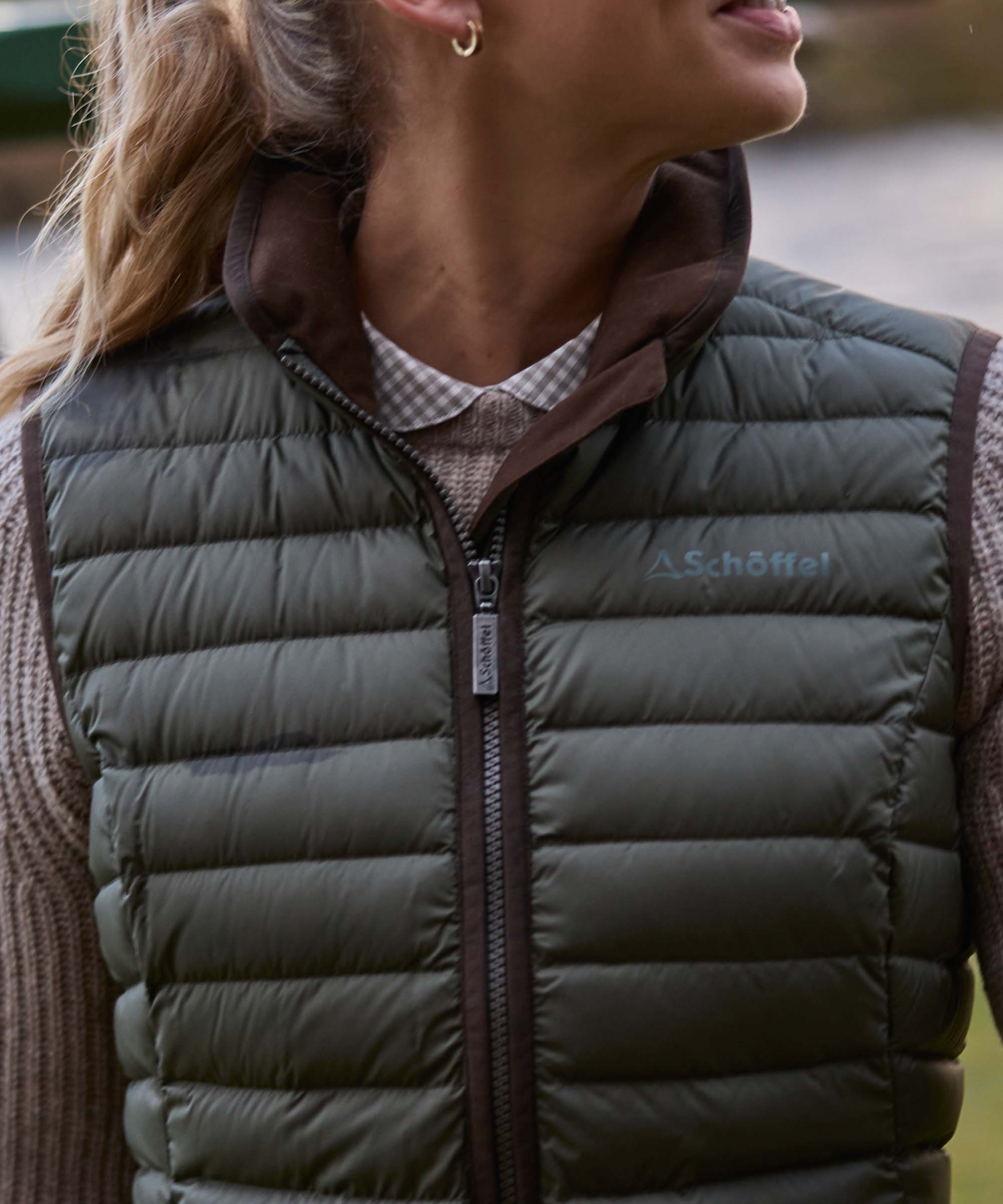 Close-up of an olive green Schöffel quilted gilet collar with zip pull and embroidered logo.