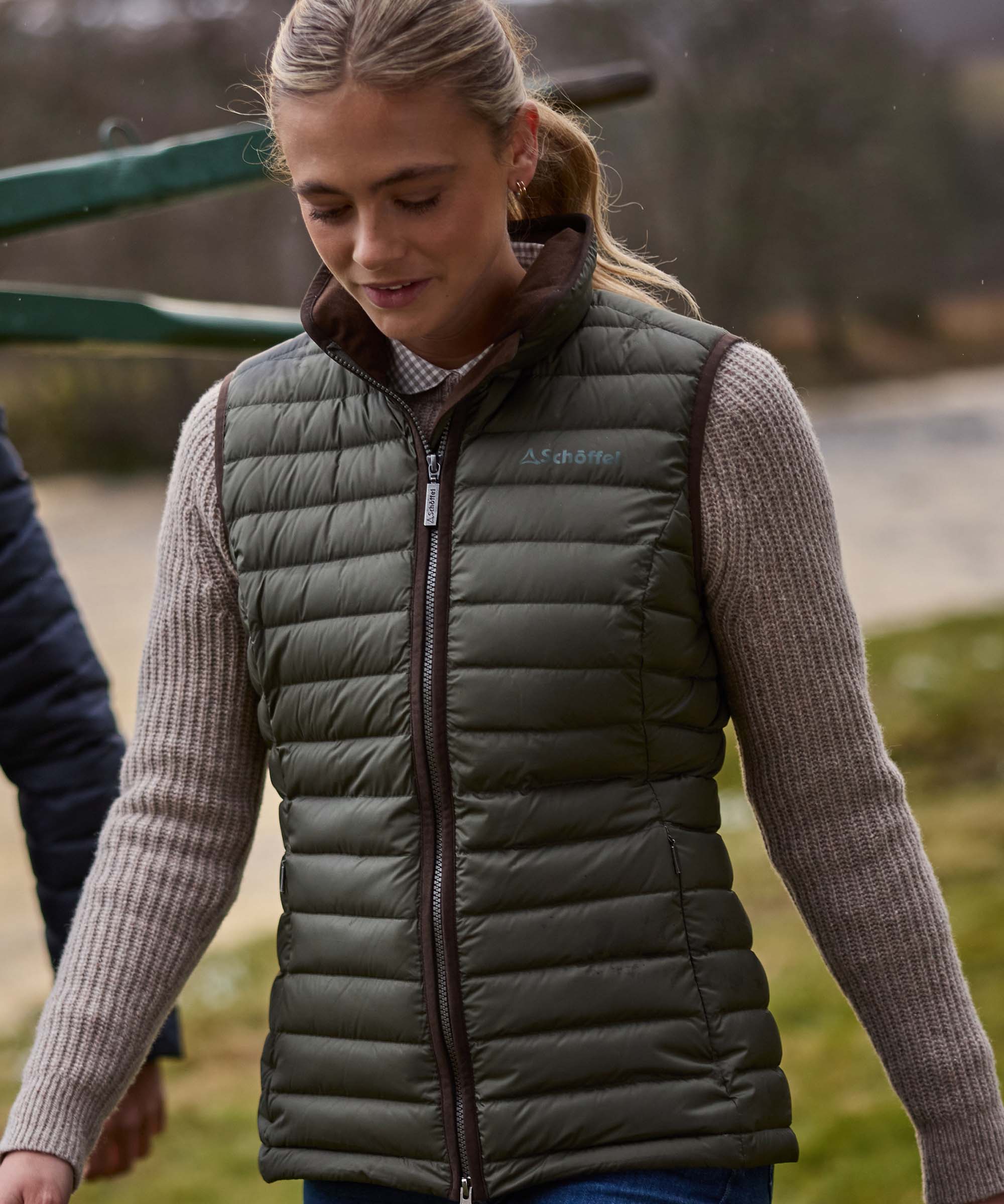 Woman wearing an olive green Schöffel quilted gilet over a knitted jumper, walking outdoors.