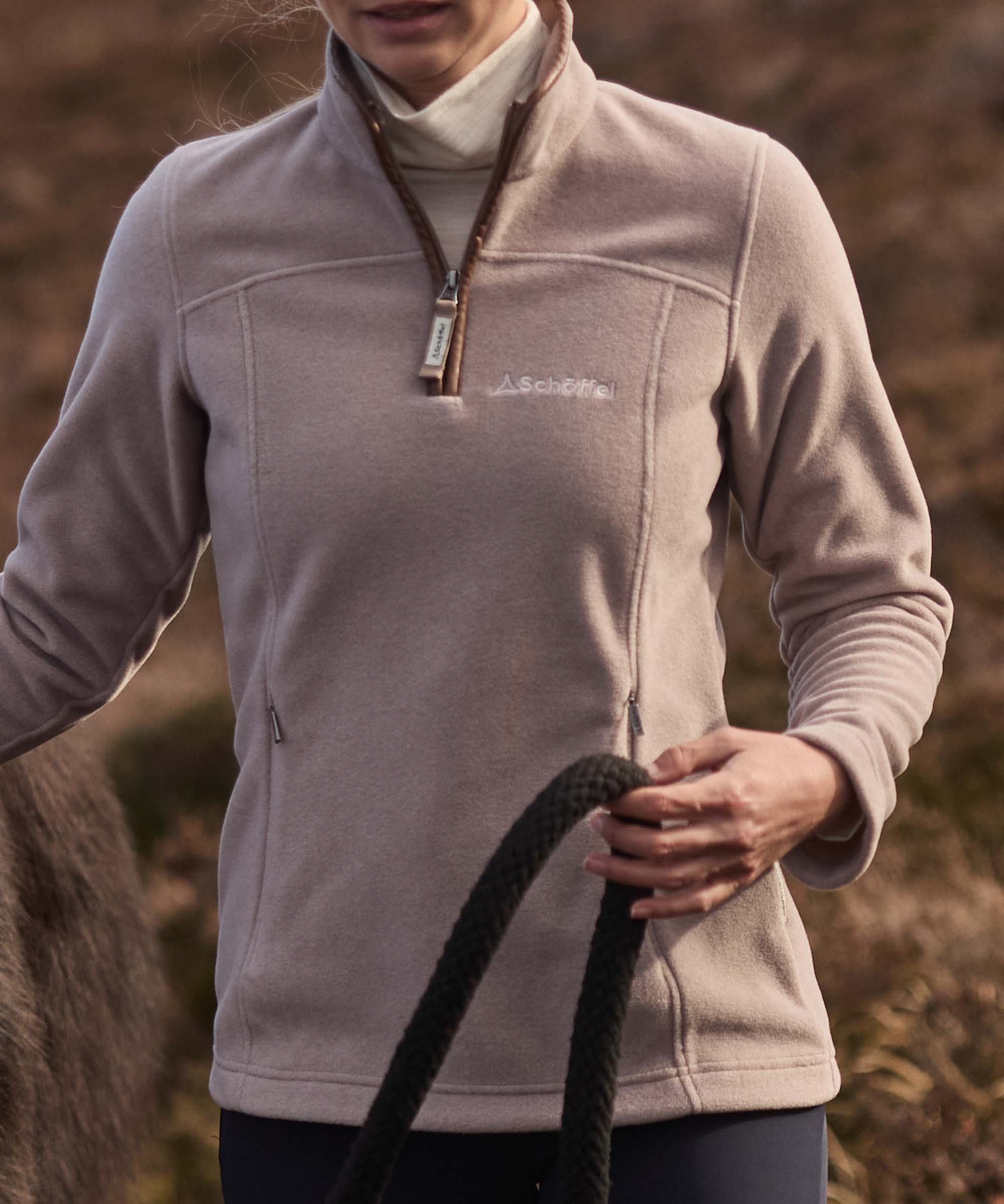 Close-up of a taupe Schöffel fleece quarter-zip chest zip and embroidered logo, holding a lead rope.