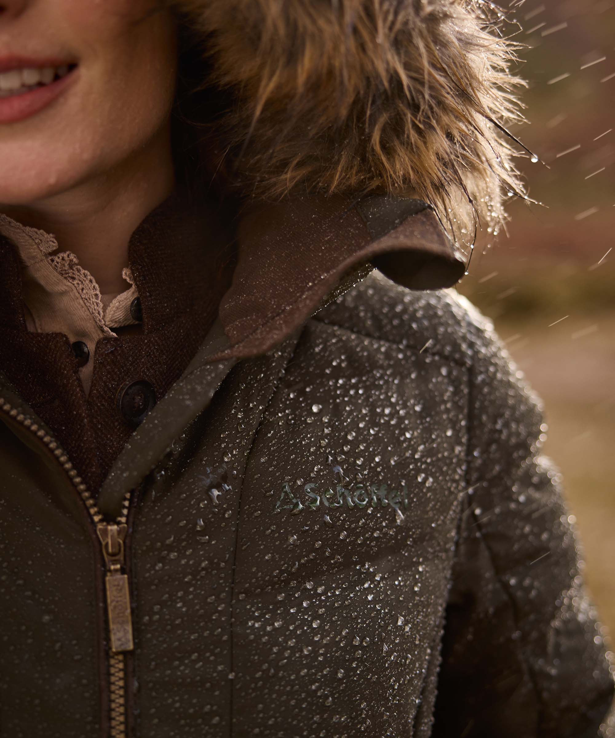 Close-up of a person wearing a dark brown hooded jacket with a fur-trimmed hood, photographed outdoors in warm natural light.