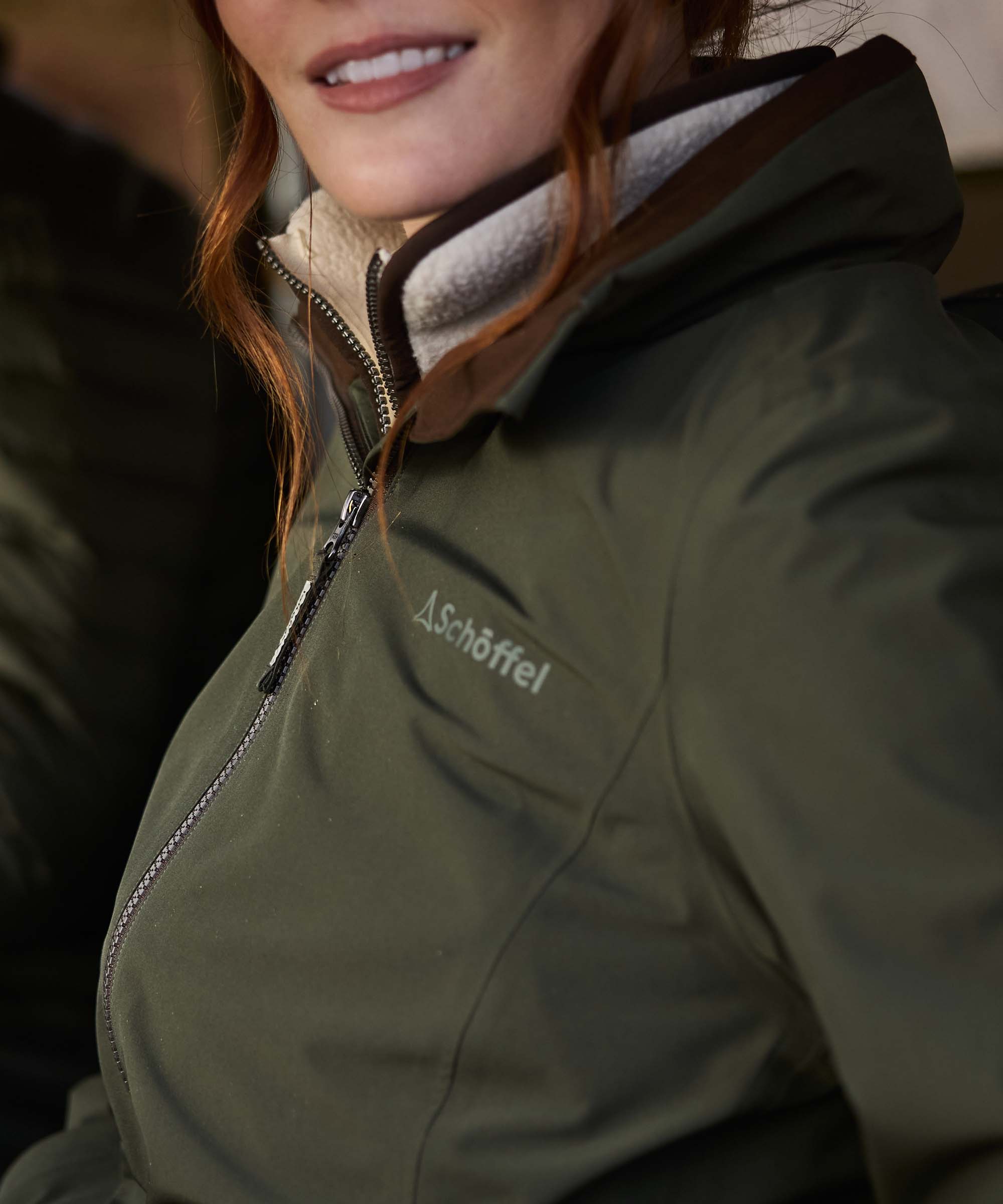 Close-up of olive green women's waterproof jacket showing brown suede collar and cream sherpa fleece lining