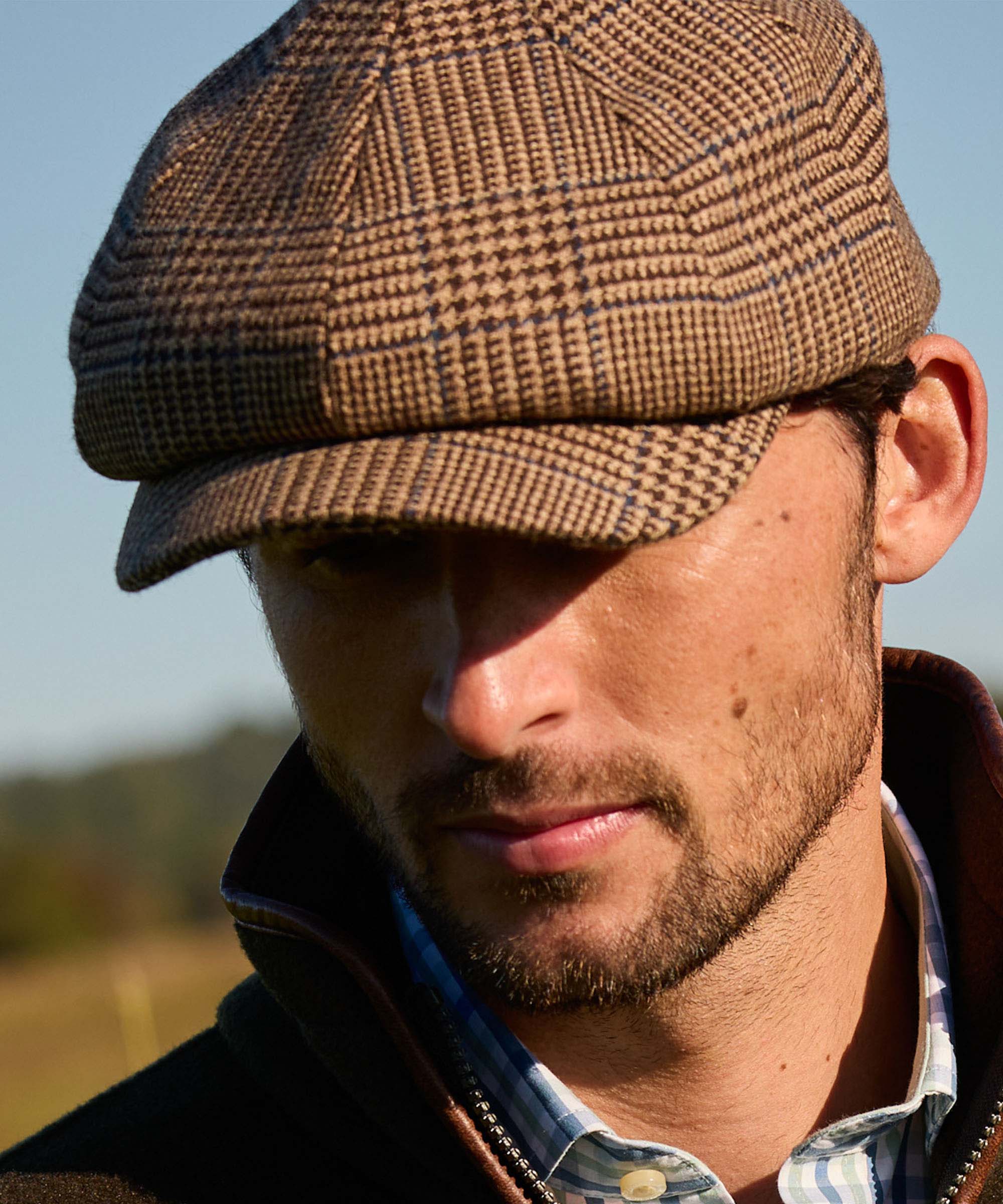 Man wearing a brown tweed flat cap outdoors with a blurred natural background