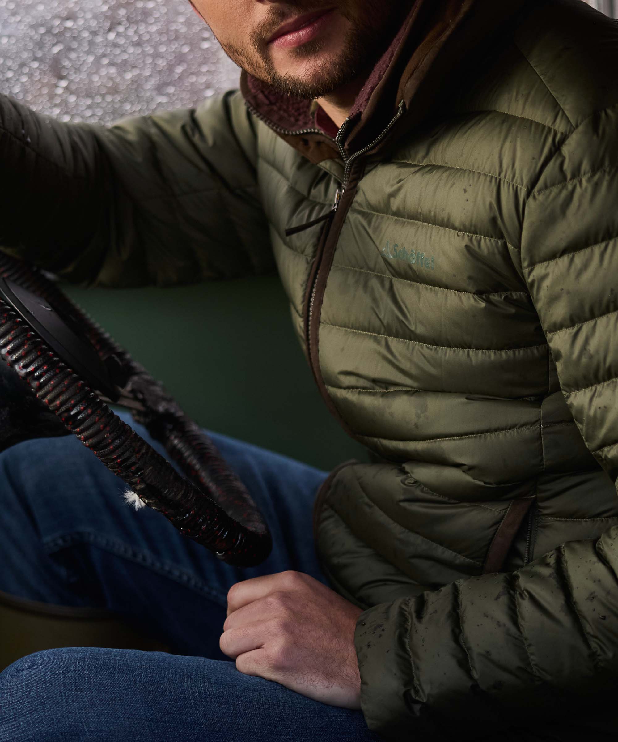 Close-up of olive green quilted down jacket with brown suede zip trim, man holding a fishing rod
