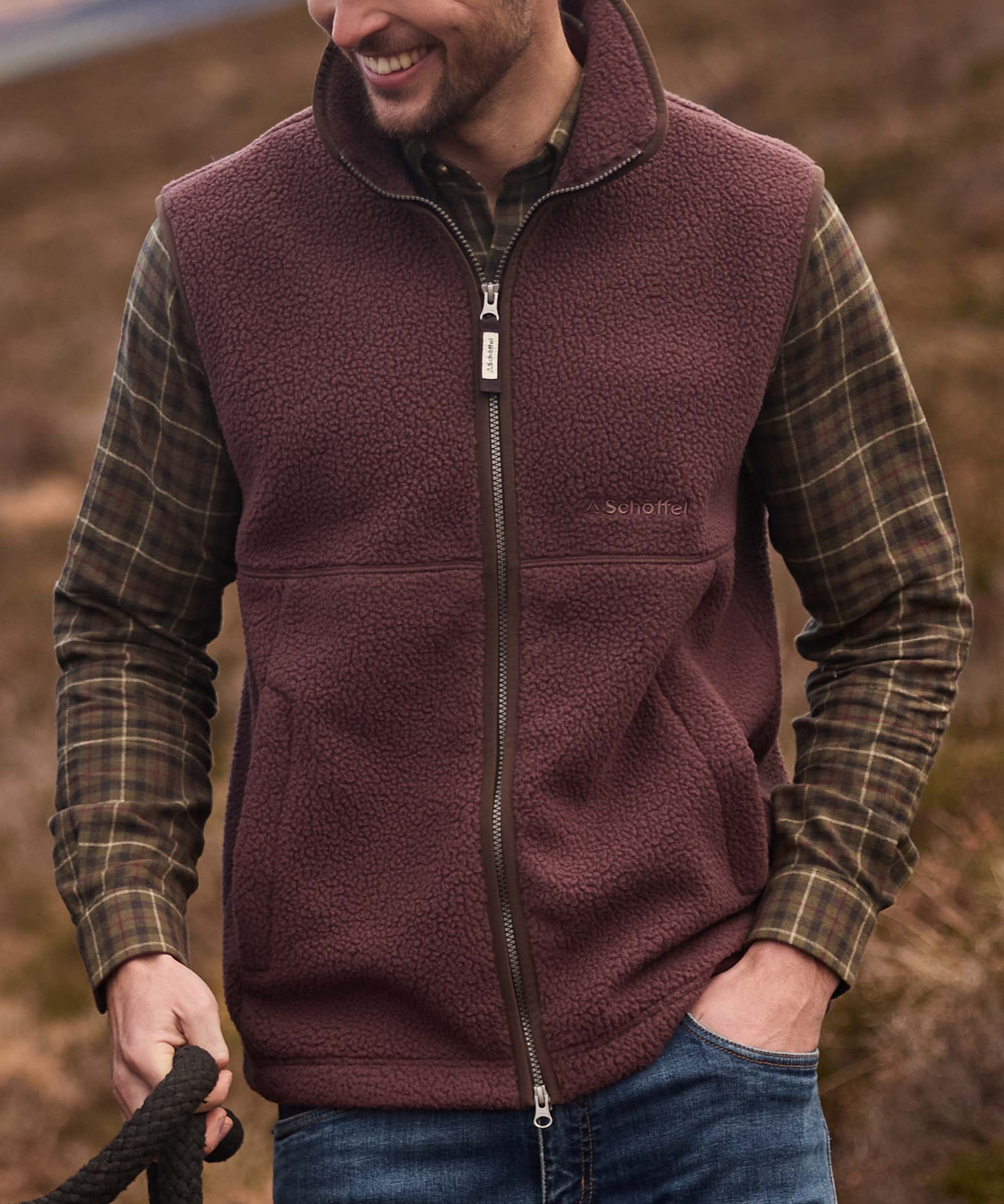 Man smiling in burgundy sherpa fleece gilet layered over tartan shirt, holding a lead rope