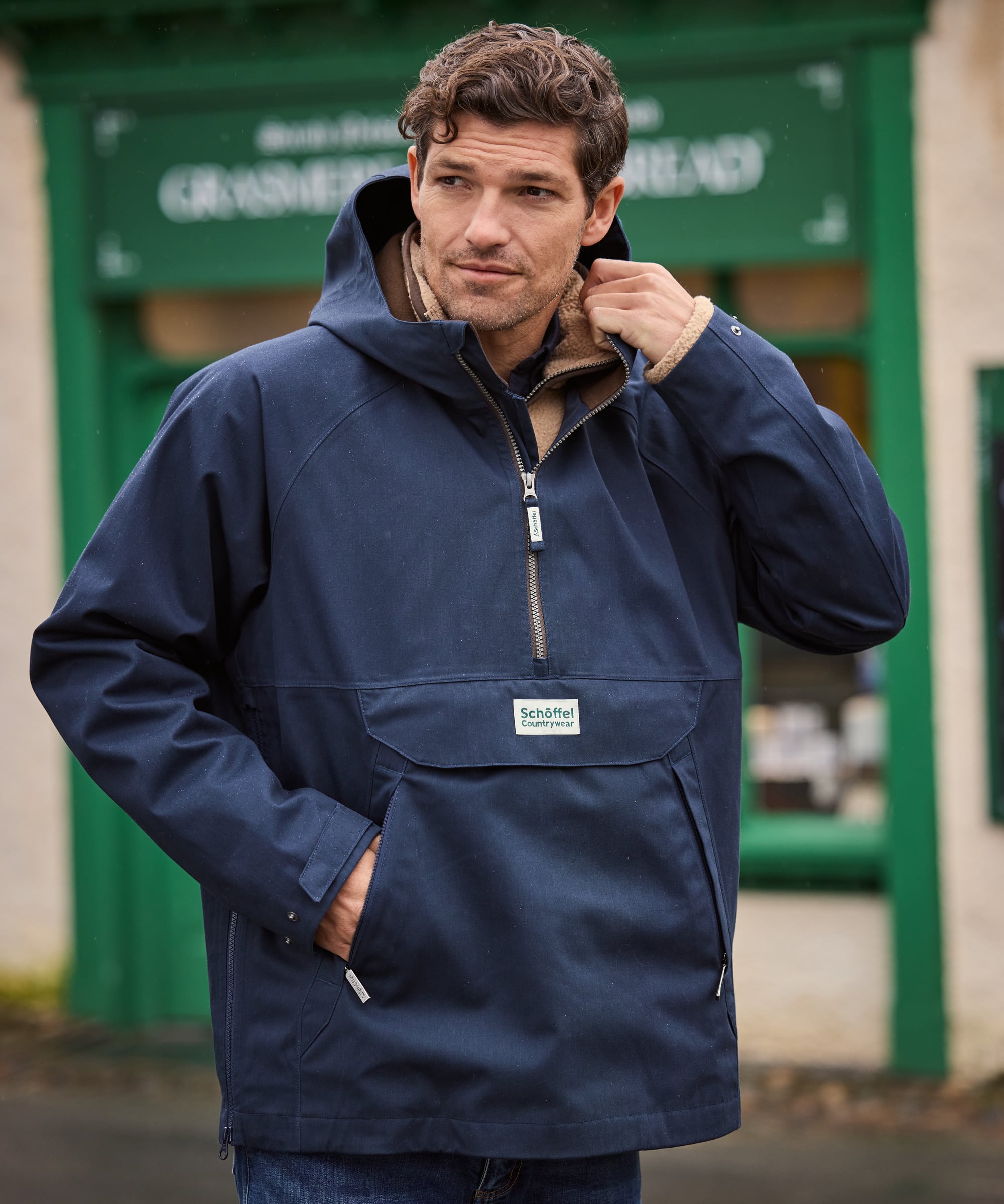 Man wearing a navy blue jacket with a brand logo, standing in front of a green building.