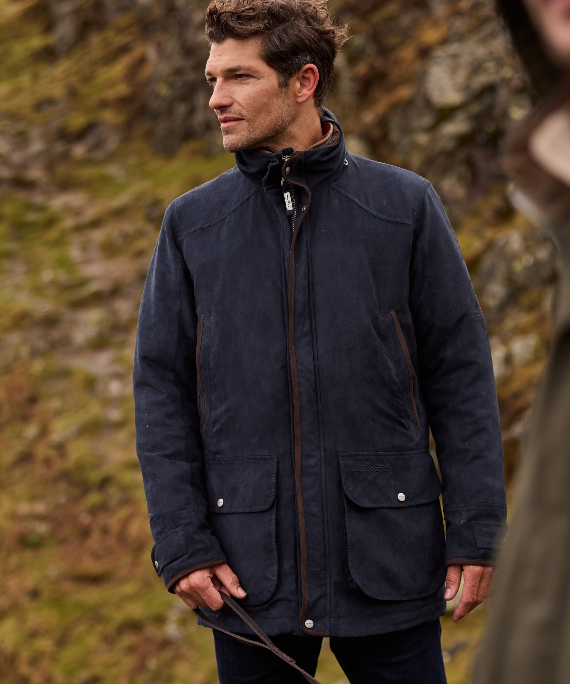 Man wearing a navy blue jacket standing outdoors with a stone wall background