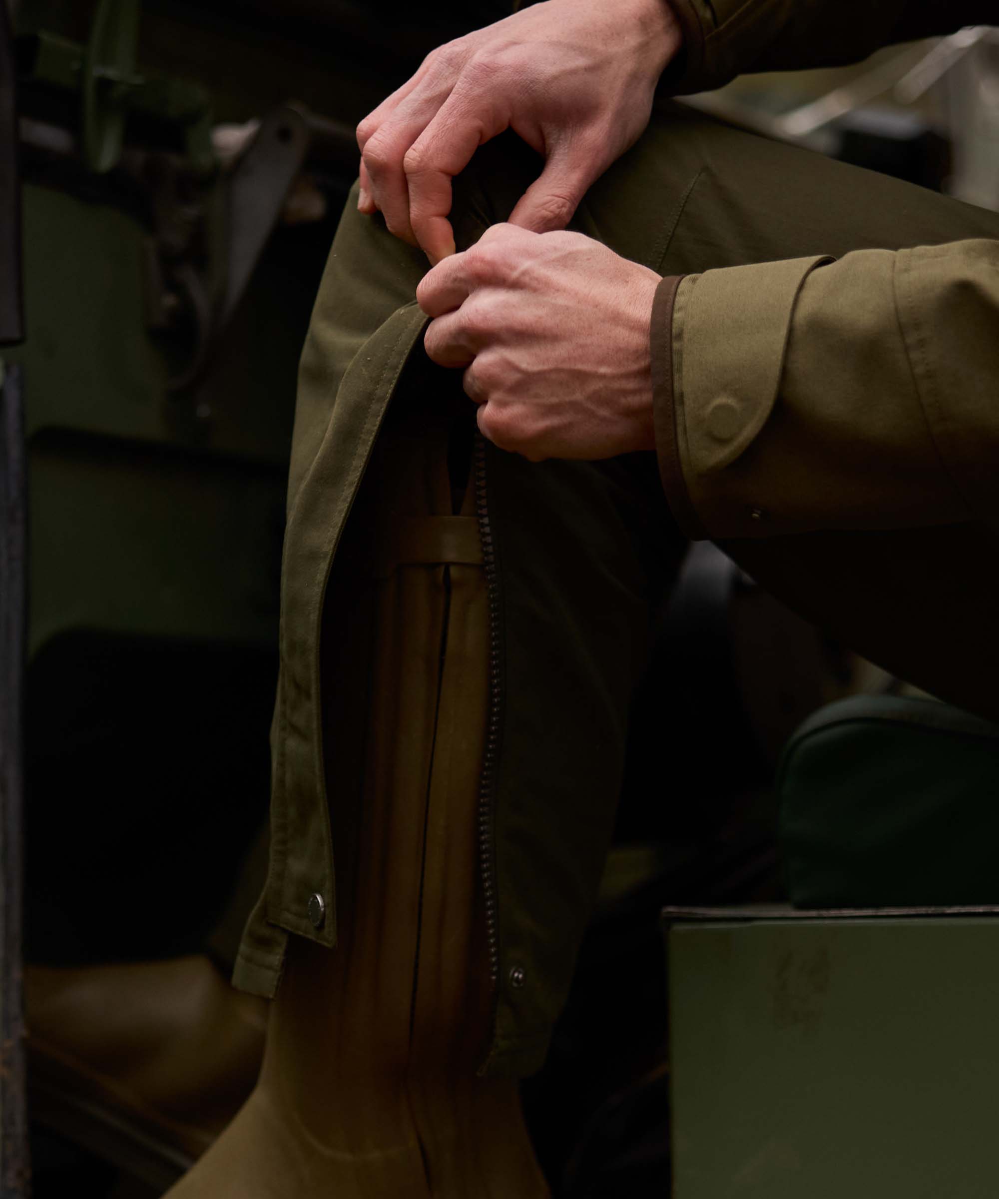 Close-up of a hand fastening the popper on an olive green Schöffel jacket pocket flap.