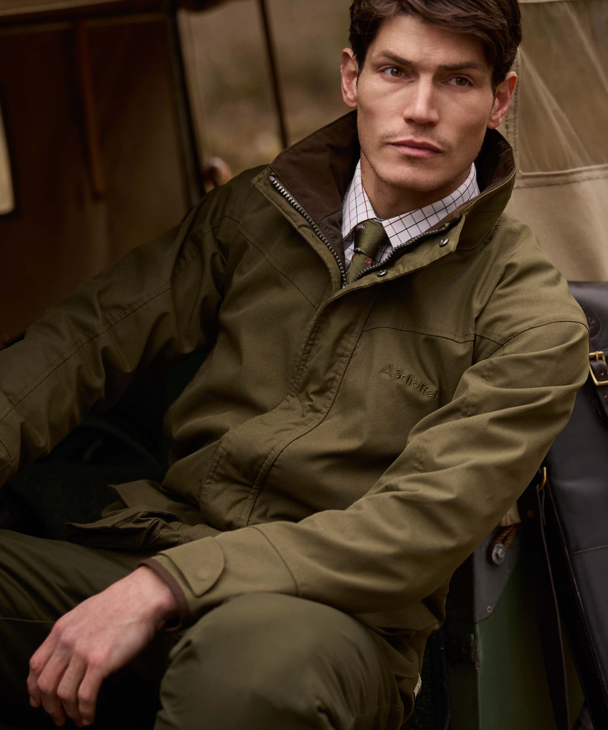 Man sat in a vintage vehicle wearing an olive green Schöffel jacket with brown corduroy collar over a checked shirt.