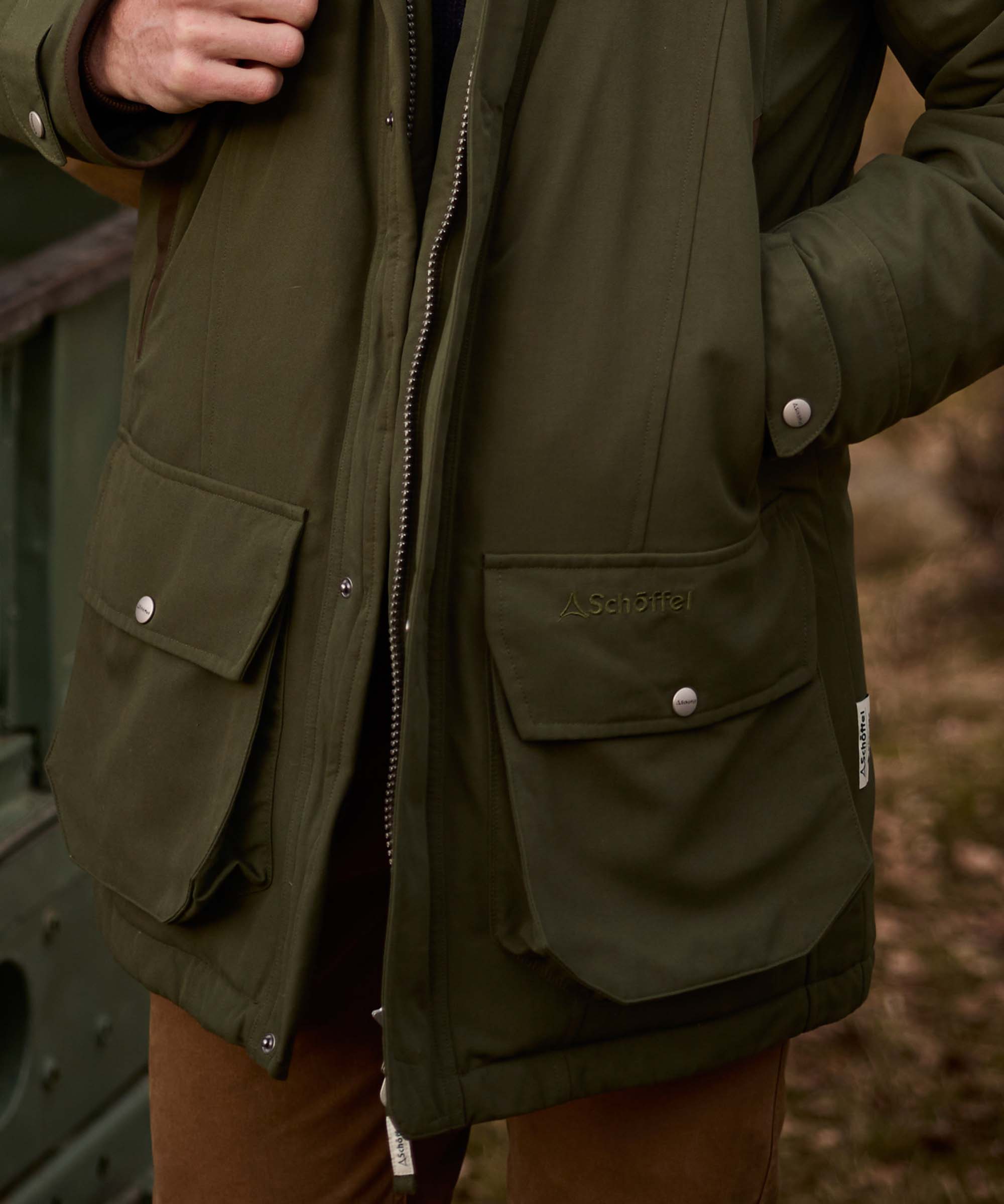 Close-up of an olive green Schöffel jacket pocket detail, showing popper fastenings and branded flap.