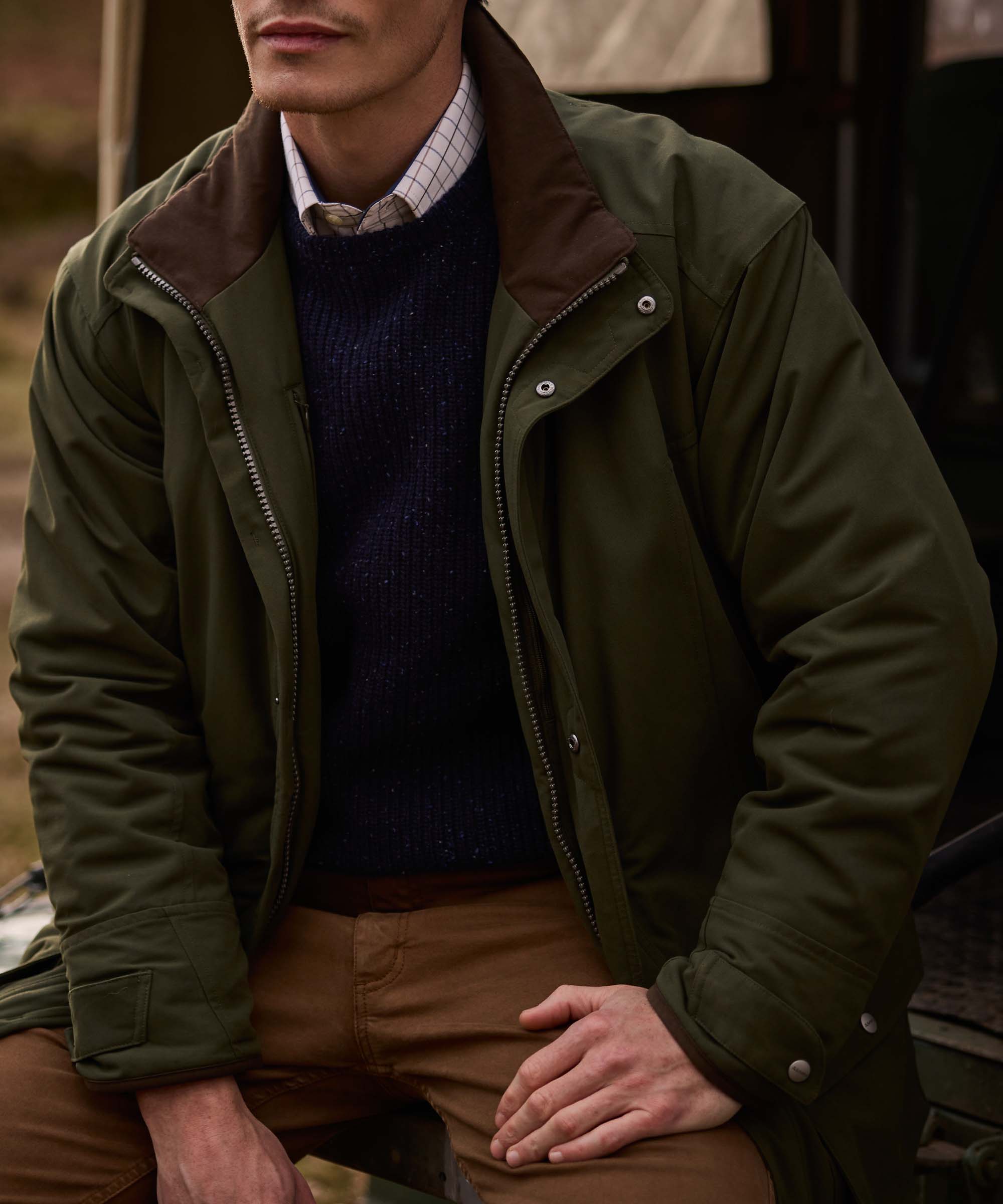 Close-up of an olive green Schöffel jacket layered over a navy jumper and checked shirt, with brown corduroy collar detailing.