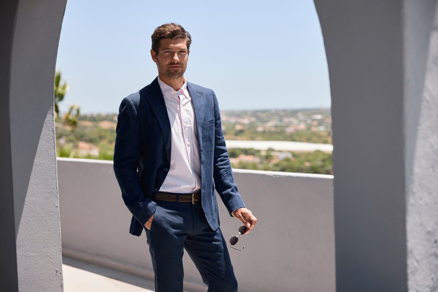 Man in a blue suit standing on a balcony with a scenic view