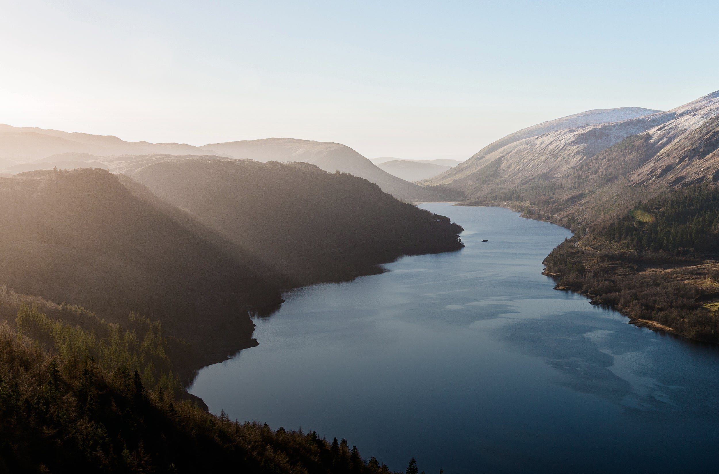 Lake surrounded by mountains and forest under a clear sky