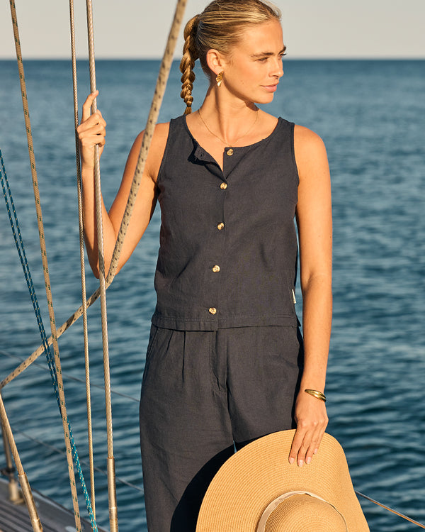 Woman in a navy sleeveless linen  top and trousers standing on a boat with water in the background