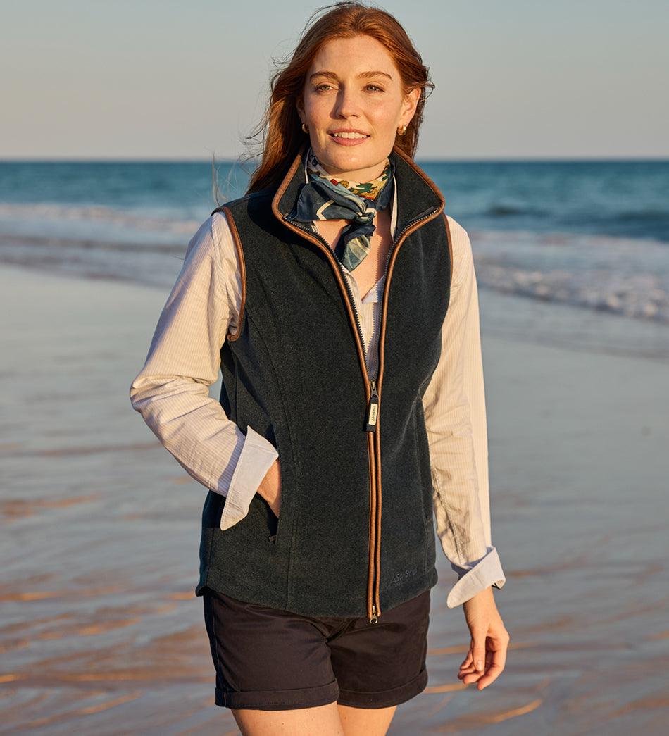 Woman standing on a beach wearing a Navy Oakham Gilet and silk scarf