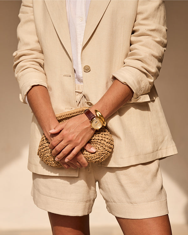 Person wearing a beige linen co-ord holding a woven clutch with a plain background