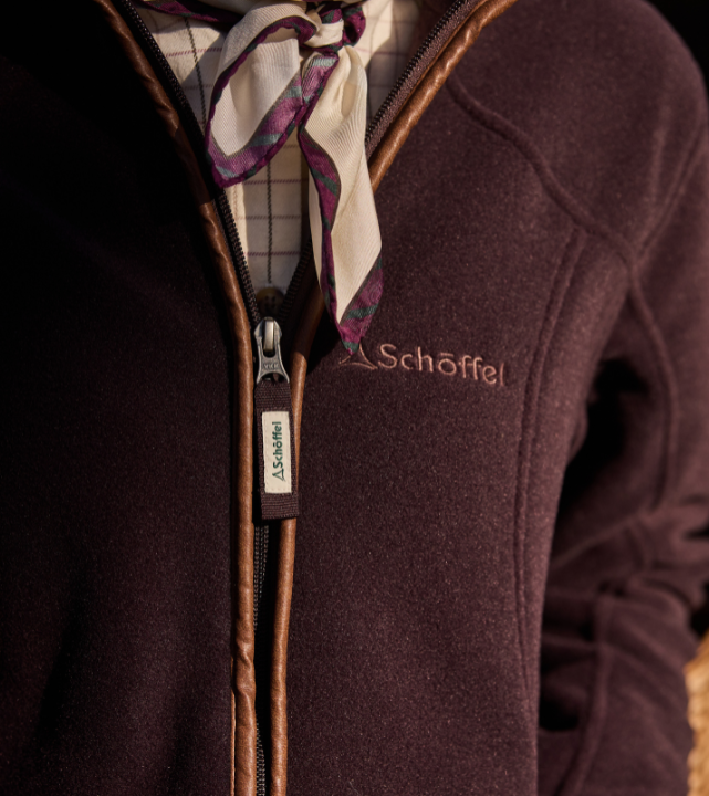 Close-up of a deep burgundy fleece jacket with contrast trim, showing the Schöffel logo and zip detail.