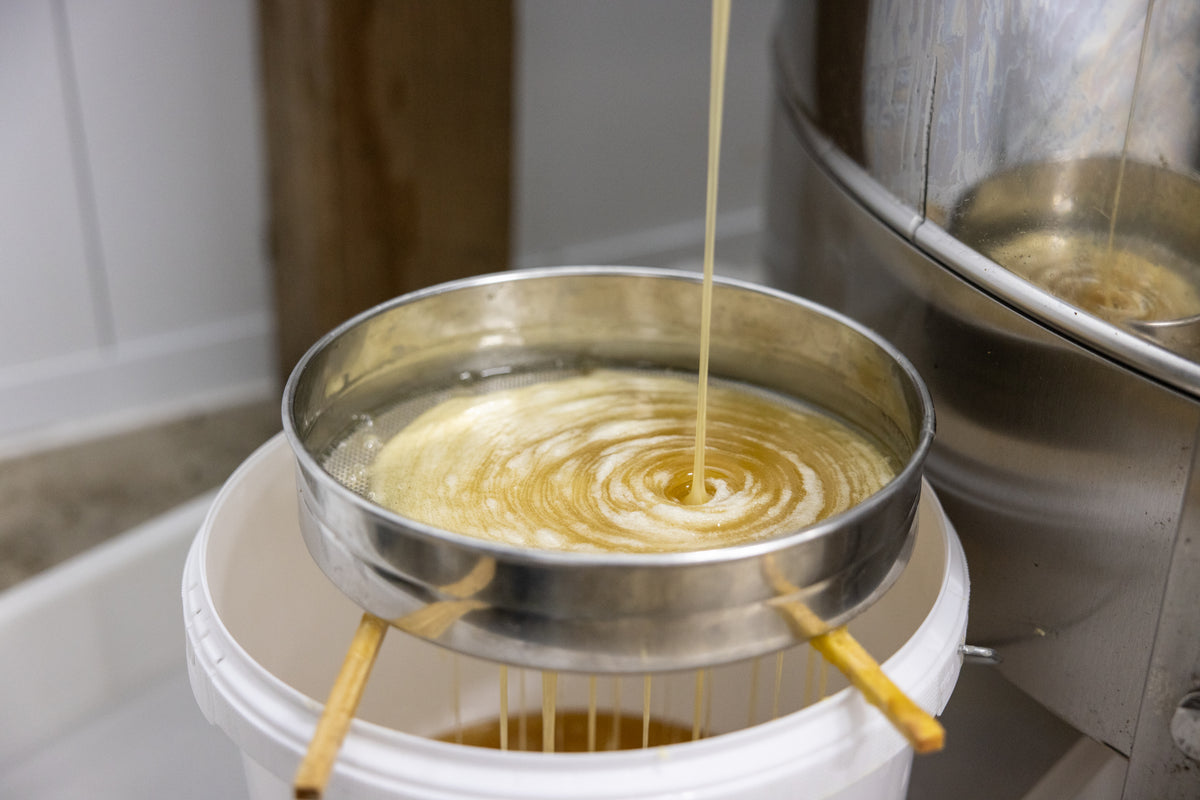 A tin of honey being strained in a factory.
