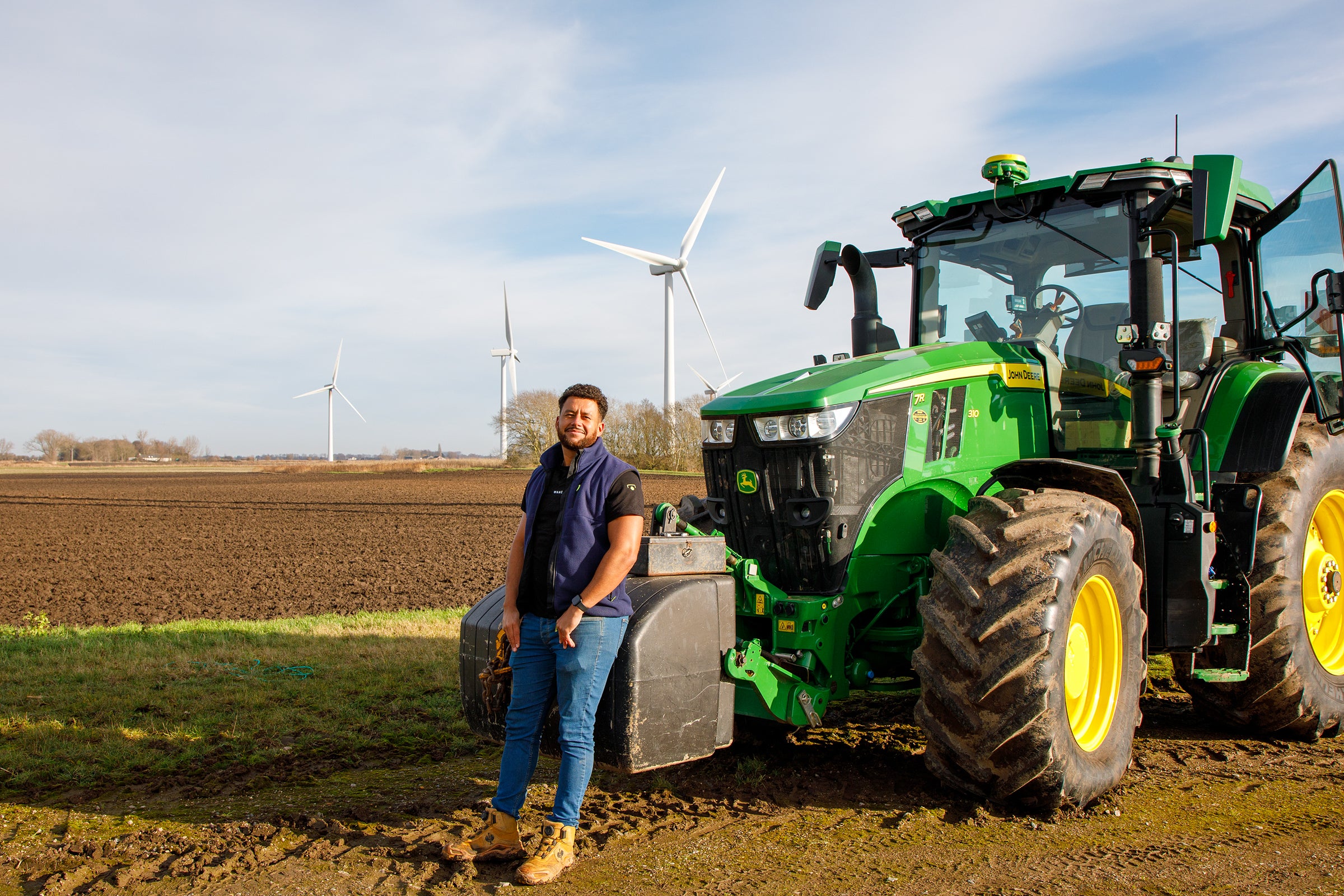 Man standing next to a green tractor in a field with wind turbines in the background