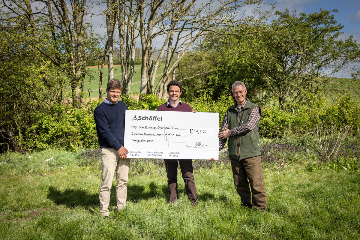 Three men standing outdoors in a grassy field, holding a large ceremonial check