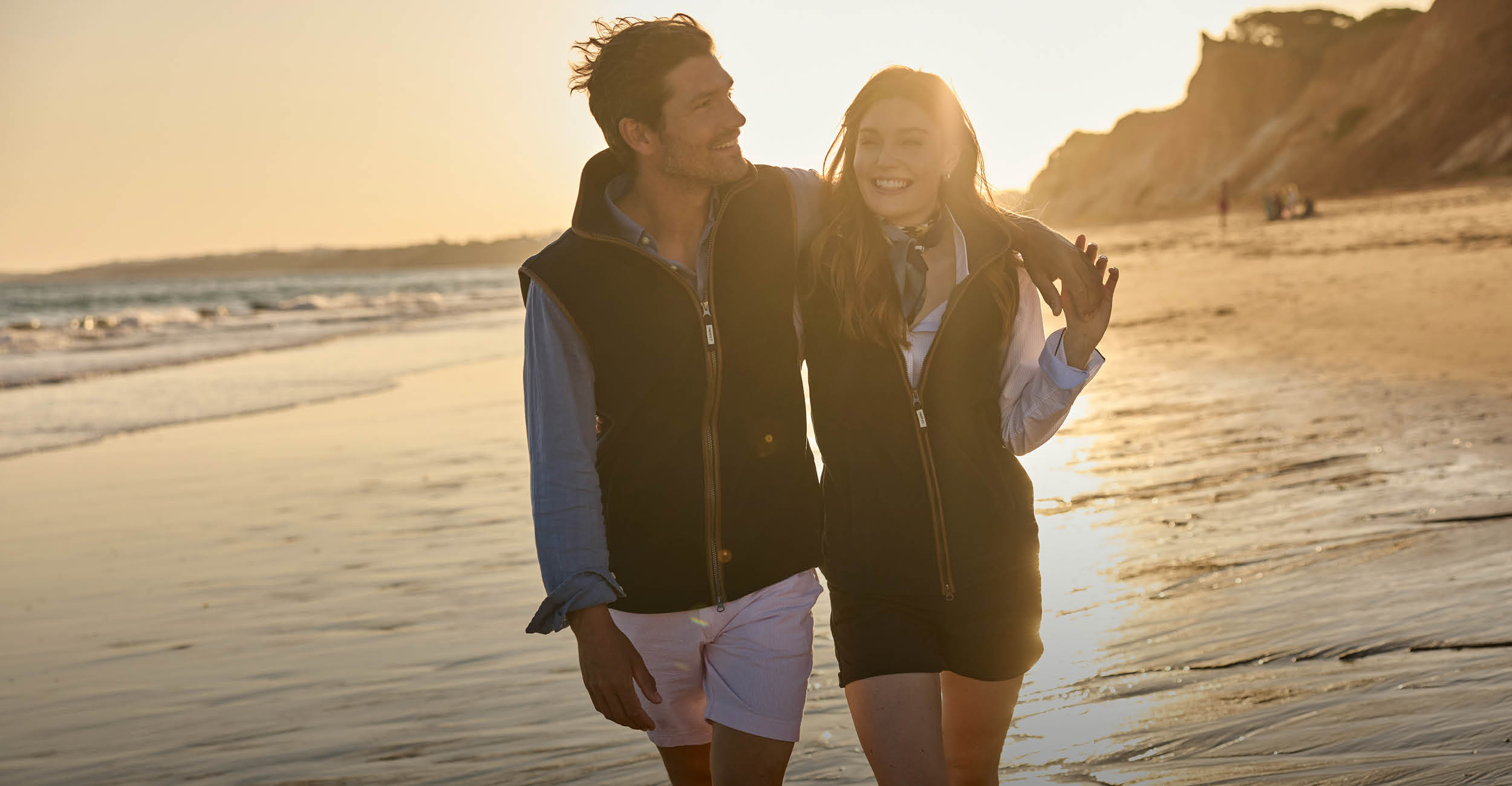 Two people walking on a beach at sunset