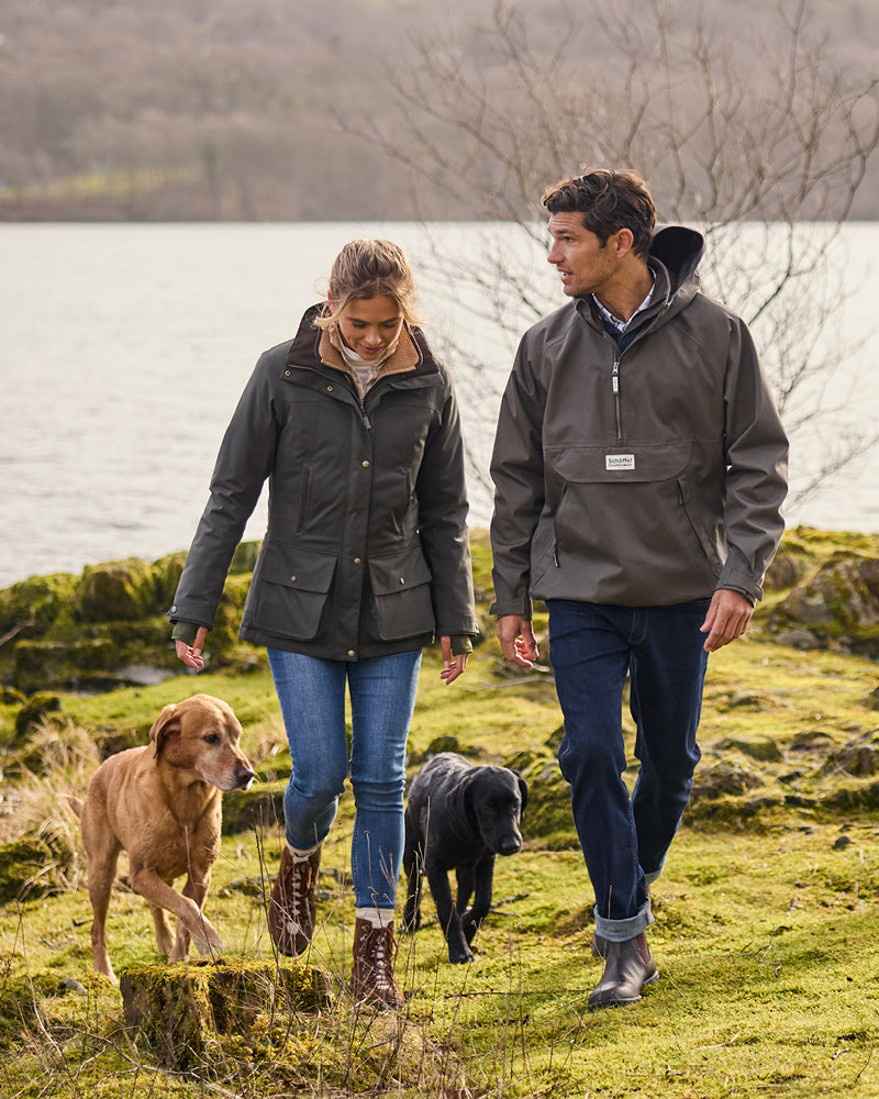 Two people walking with two dogs by a lake