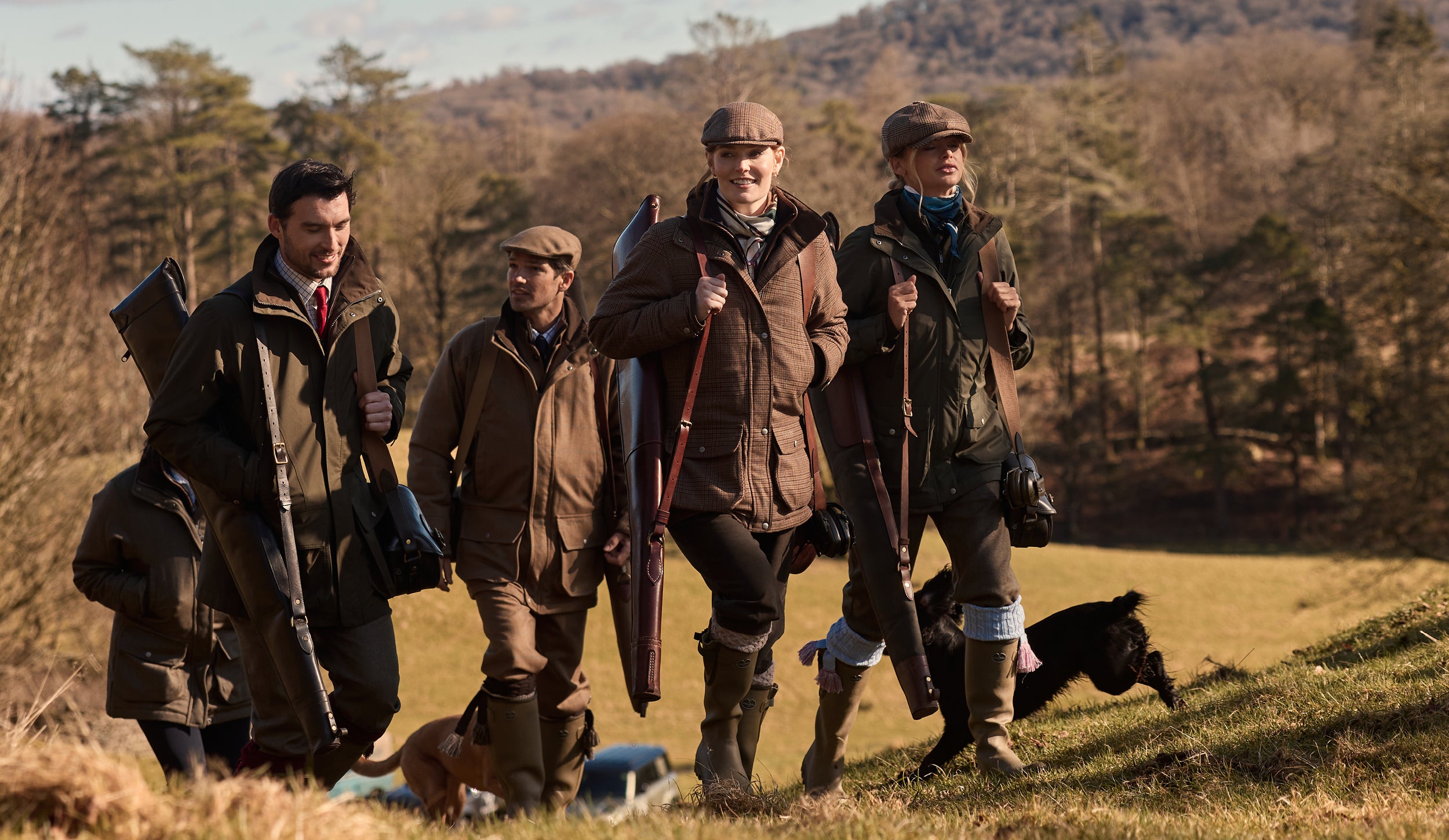 Four people in hunting attire walking with dogs in a field