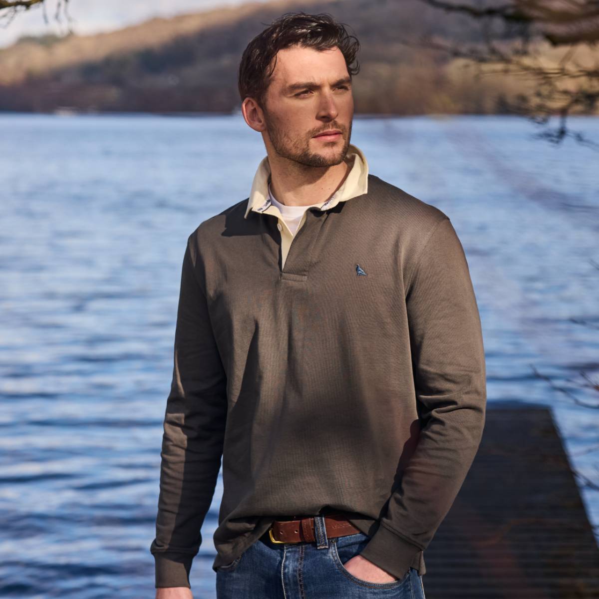 Man wearing a brown sweater with a blurred lake and trees in the background
