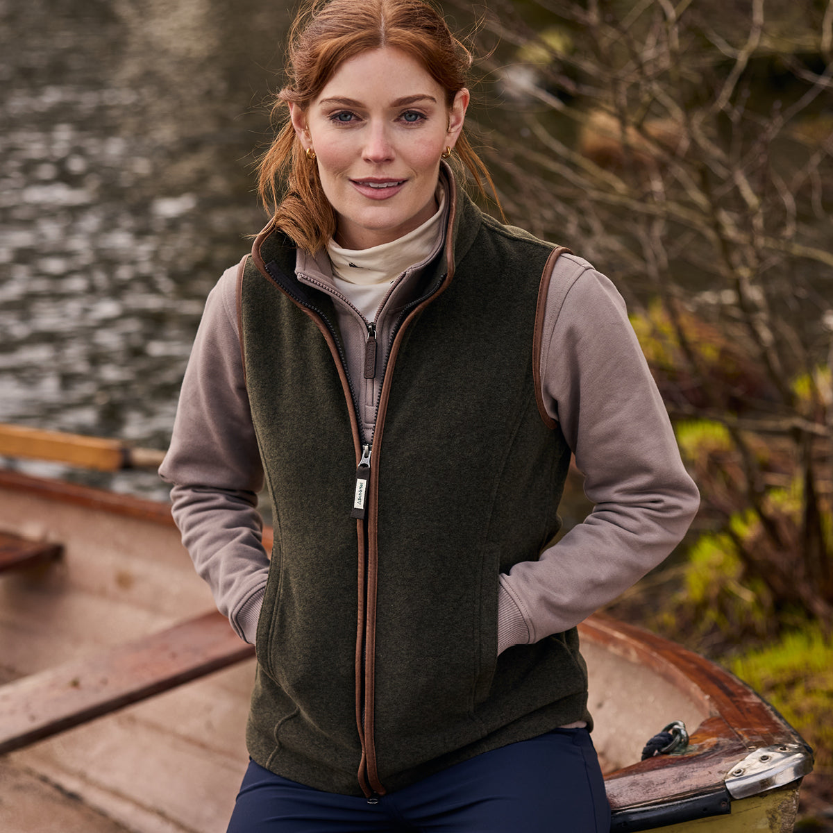 Woman wearing a green gilet over a light grey shirt with a blurred natural background