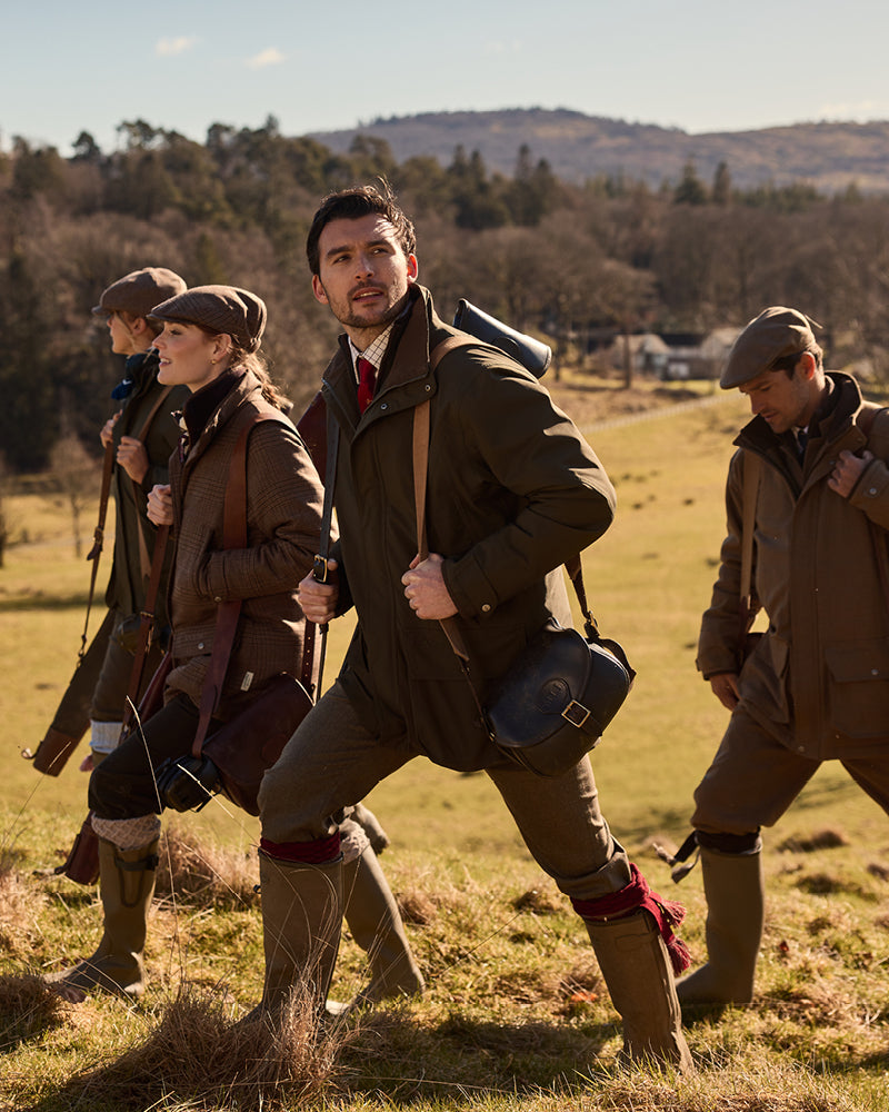 Four people in shooting attire walking through a field with a scenic background.