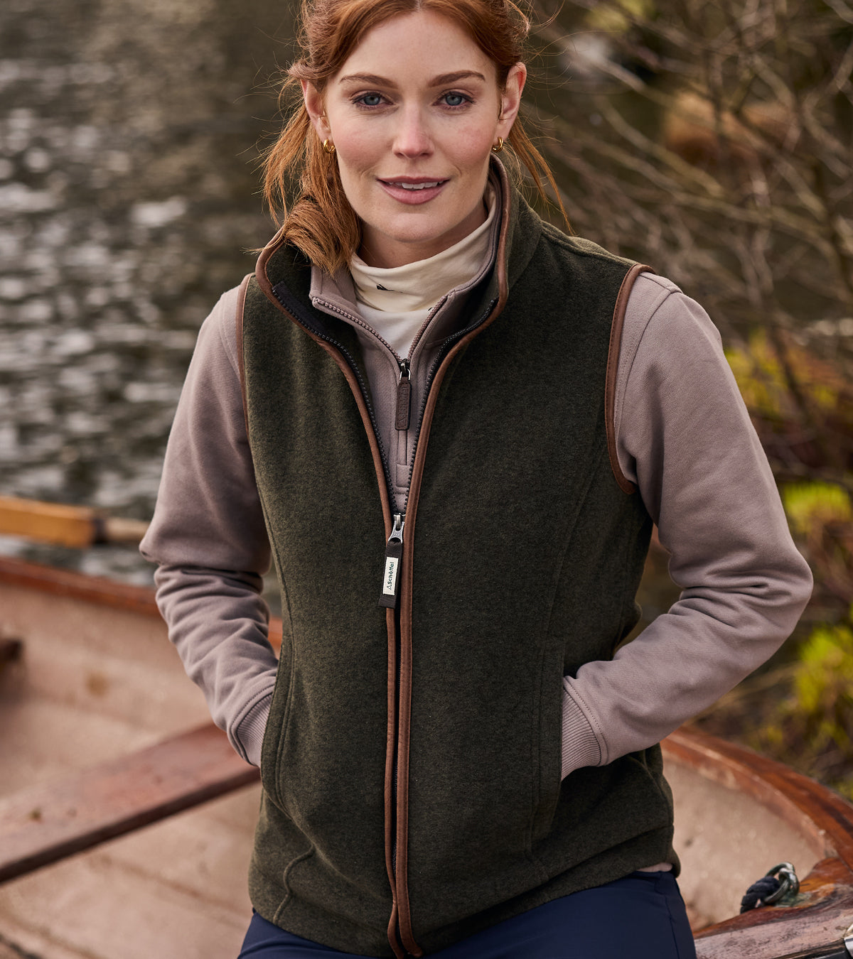 Woman wearing a green fleece gilet over a light brown sweatshirt next to a boat