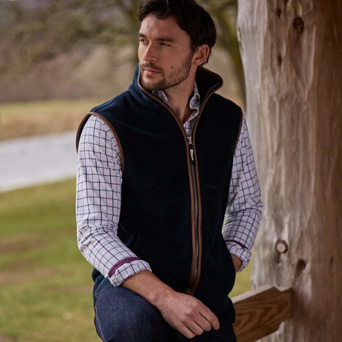 Man wearing dark navy fleece gilet over a white and blue checked shirt.