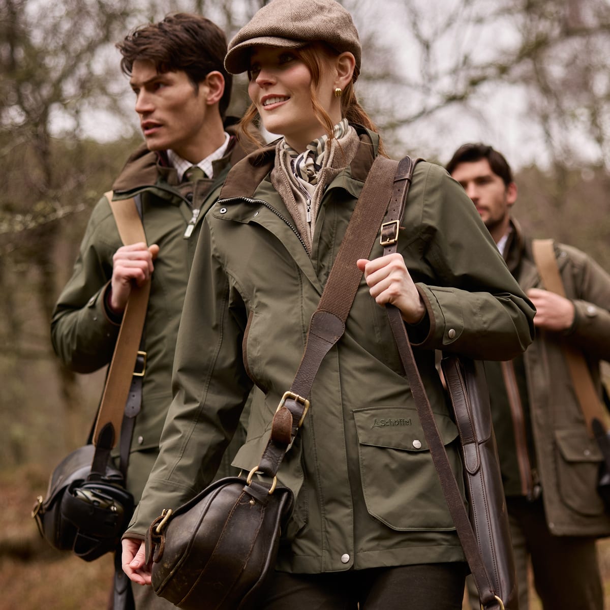 Three people outdoors wearing green shooting jackets and carrying leather bags