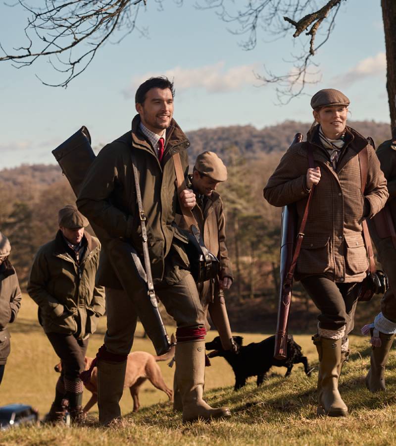 Group of people in hunting attire walking with dogs in a field