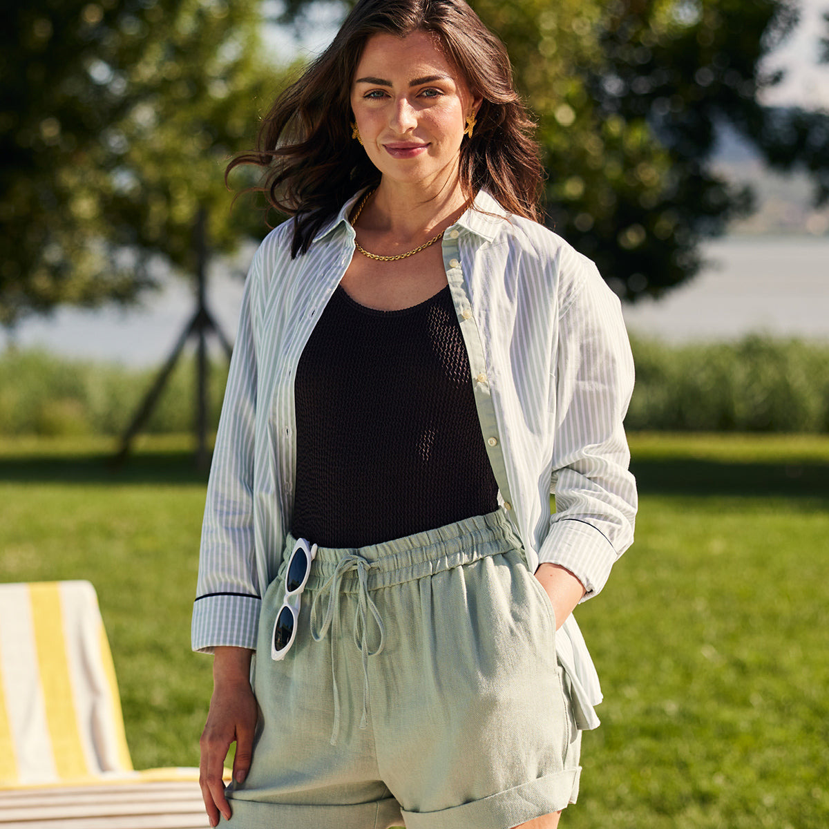 Woman standing outdoors in a park-like setting wearing a light jacket, black top, and light pants.