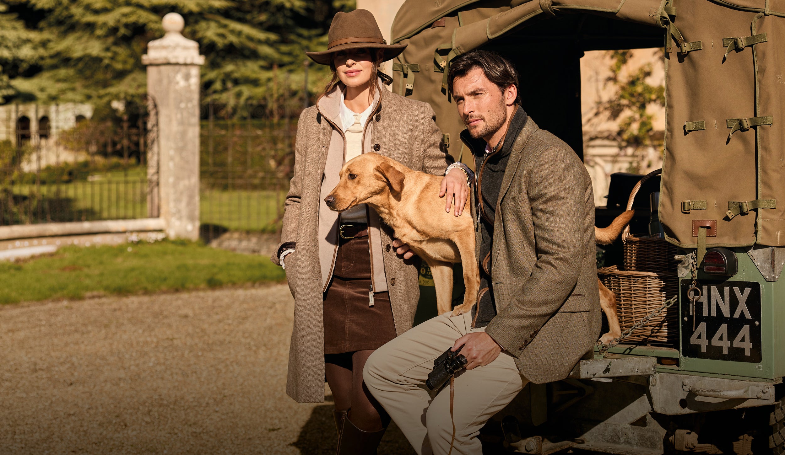 Two people with a dog in front of an open vehicle in a scenic area.